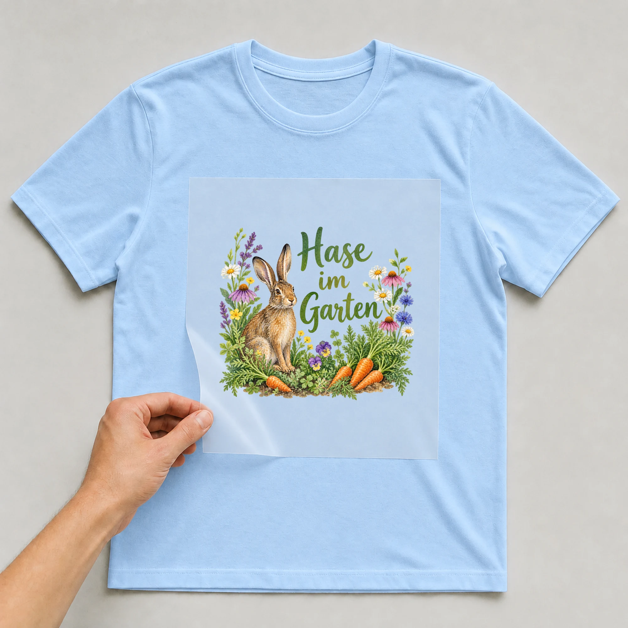Bügelbild „Hase im Garten“ auf babyblauem T-Shirt, Folie wird aufgelegt