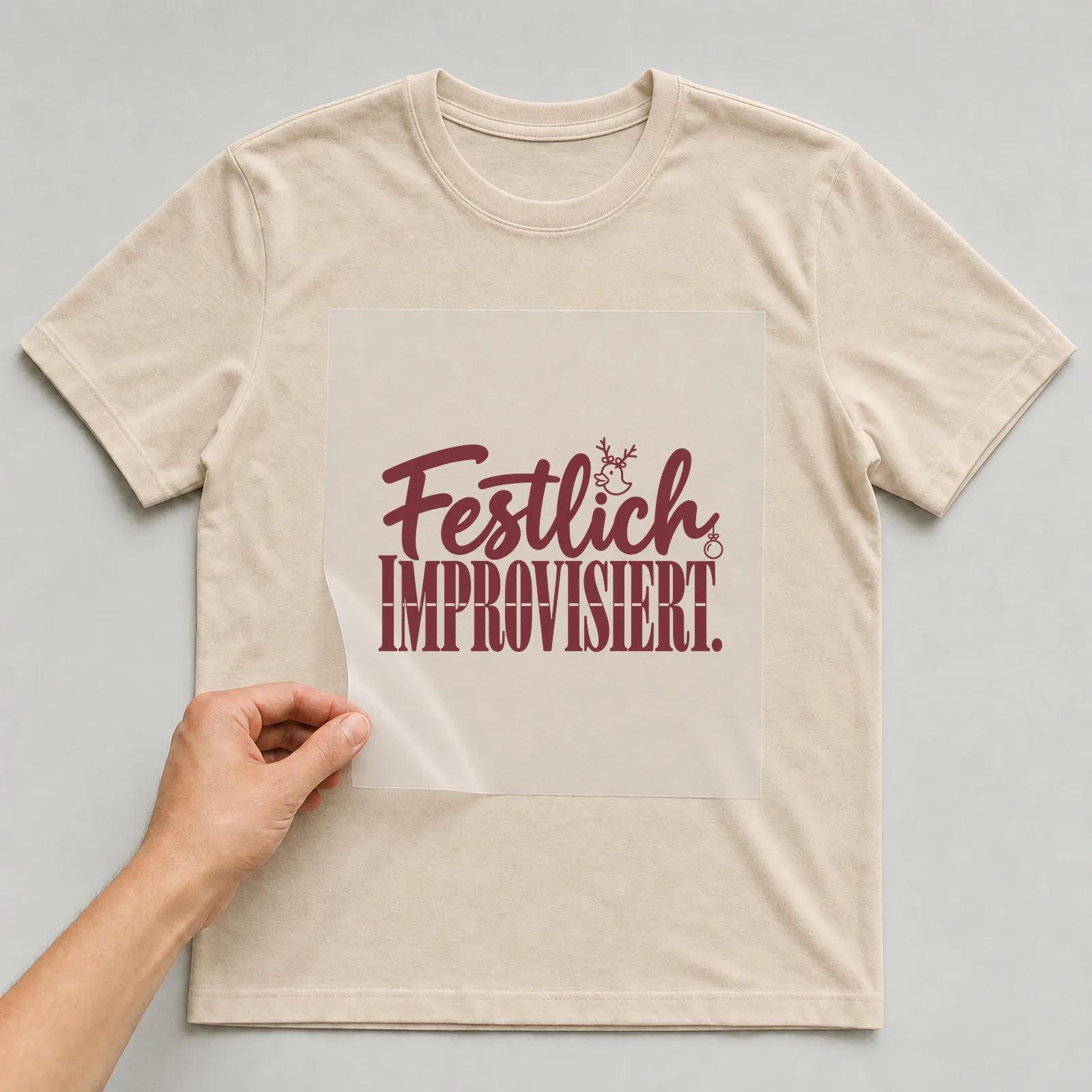 Bügelbild „Festlich improvisiert“ (Schrift Konturen) auf beigem T-Shirt, Folie wird aufgelegt