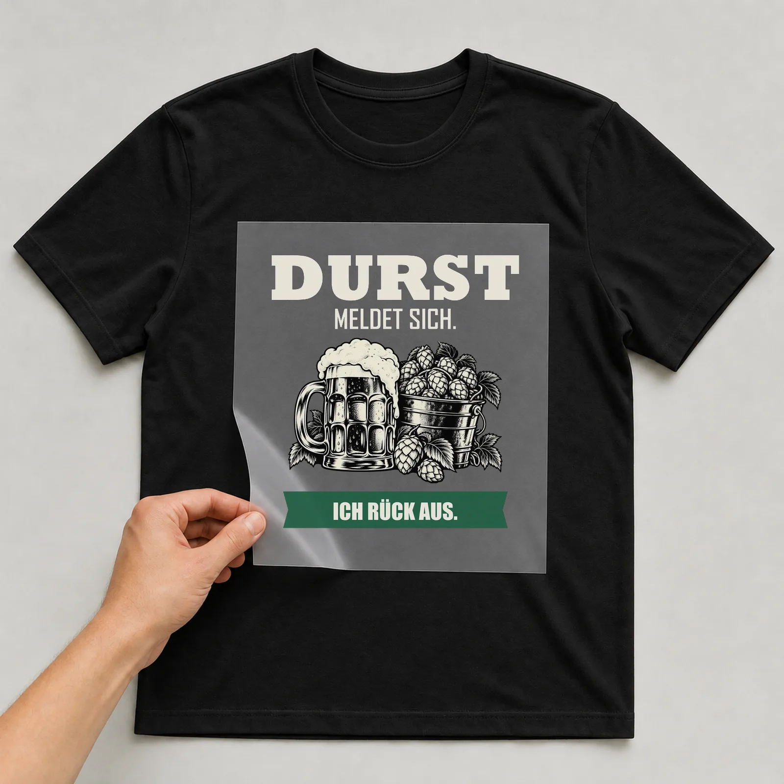 Bügelbild „Durst meldet sich. Ich rück aus.“ auf schwarzem T-Shirt, Folie wird aufgelegt
