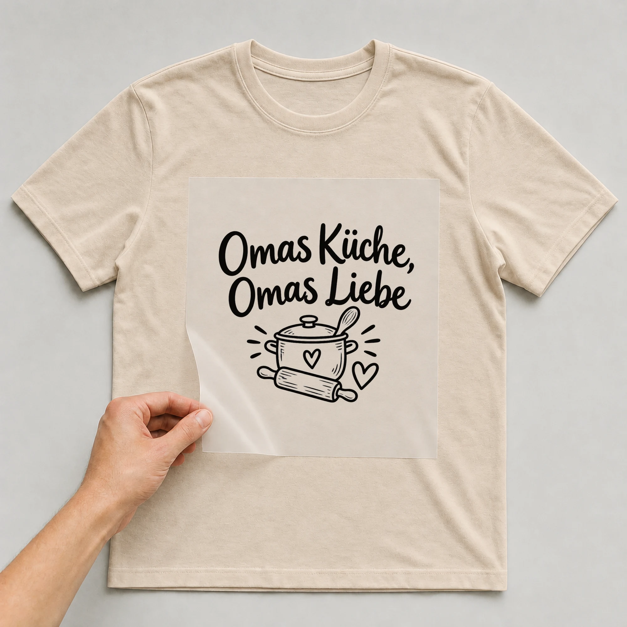 Bügelbild „Omas Küche, Omas Liebe“ auf beigem T-Shirt, Folie wird aufgelegt