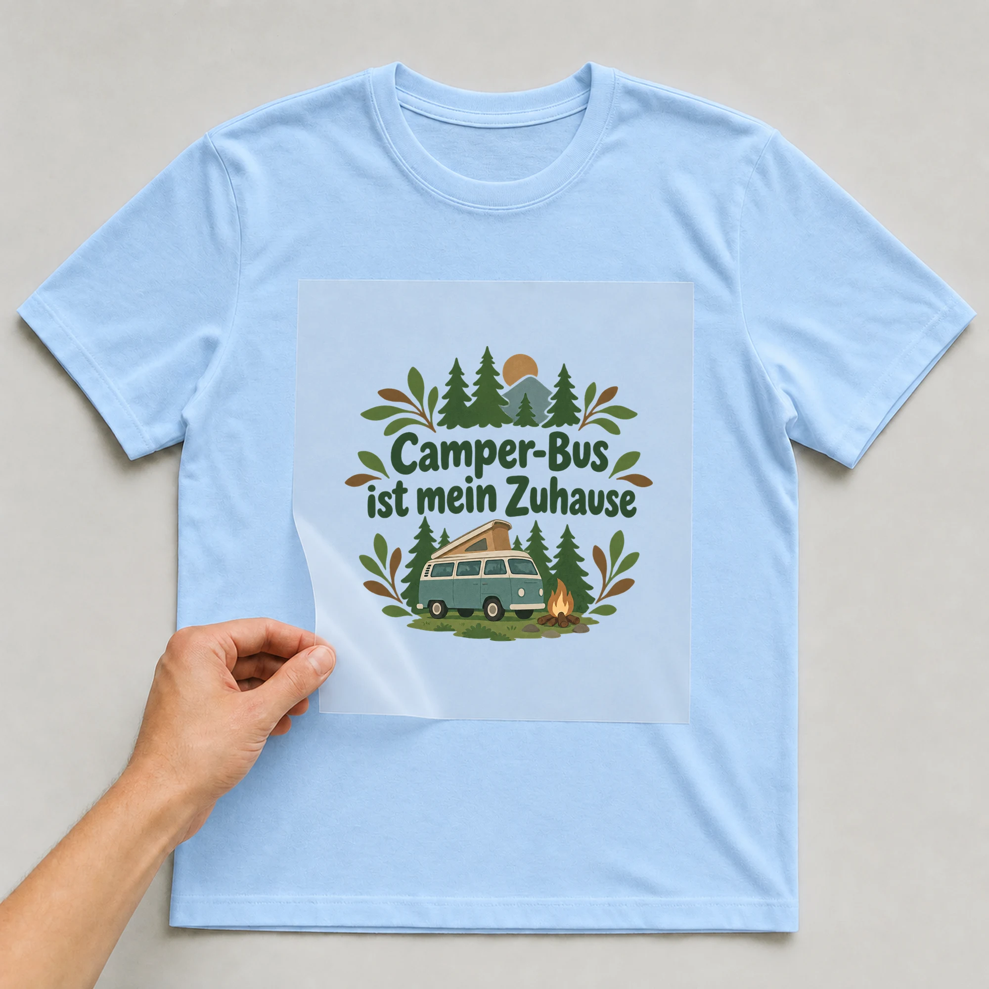 Bügelbild „Camper-Bus ist mein Zuhause“ auf babyblauem T-Shirt, Folie wird aufgelegt