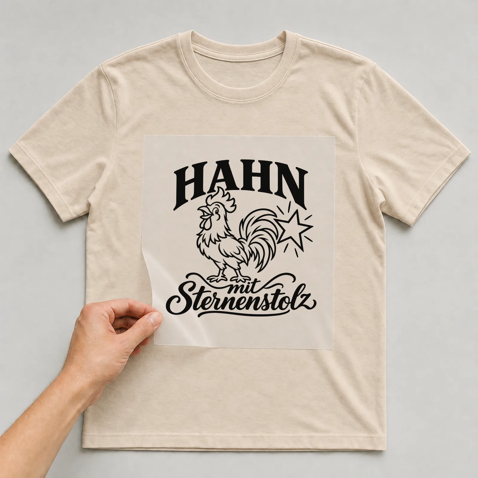 Bügelbild „Hahn mit Sternenstolz“ auf beigem T-Shirt, Folie wird aufgelegt