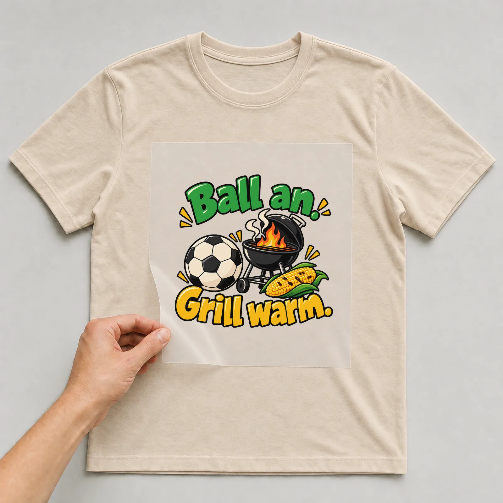 Bügelbild „Ball an. Grill warm.“ auf beigem T-Shirt, Folie wird aufgelegt