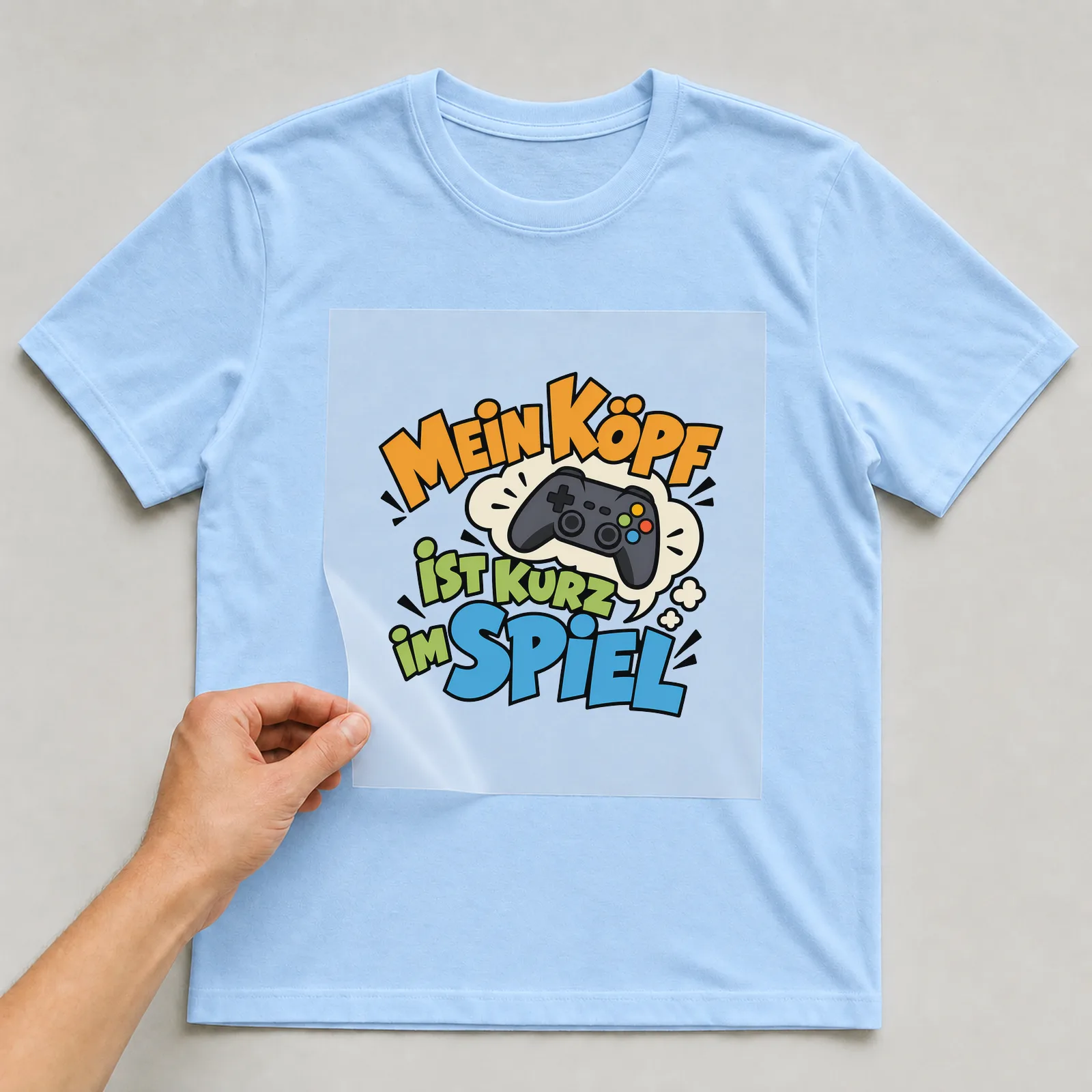 Bügelbild „Mein Kopf ist kurz im Spiel“ auf hellblauem T-Shirt, Folie wird aufgelegt