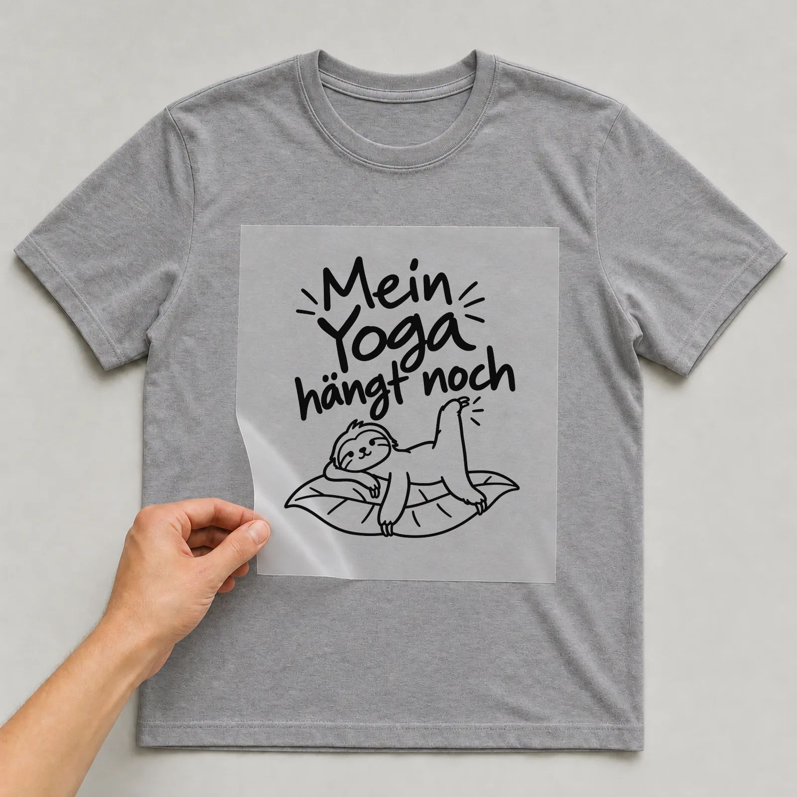 Bügelbild „Mein Yoga hängt noch“ auf grauem T-Shirt, Folie wird aufgelegt