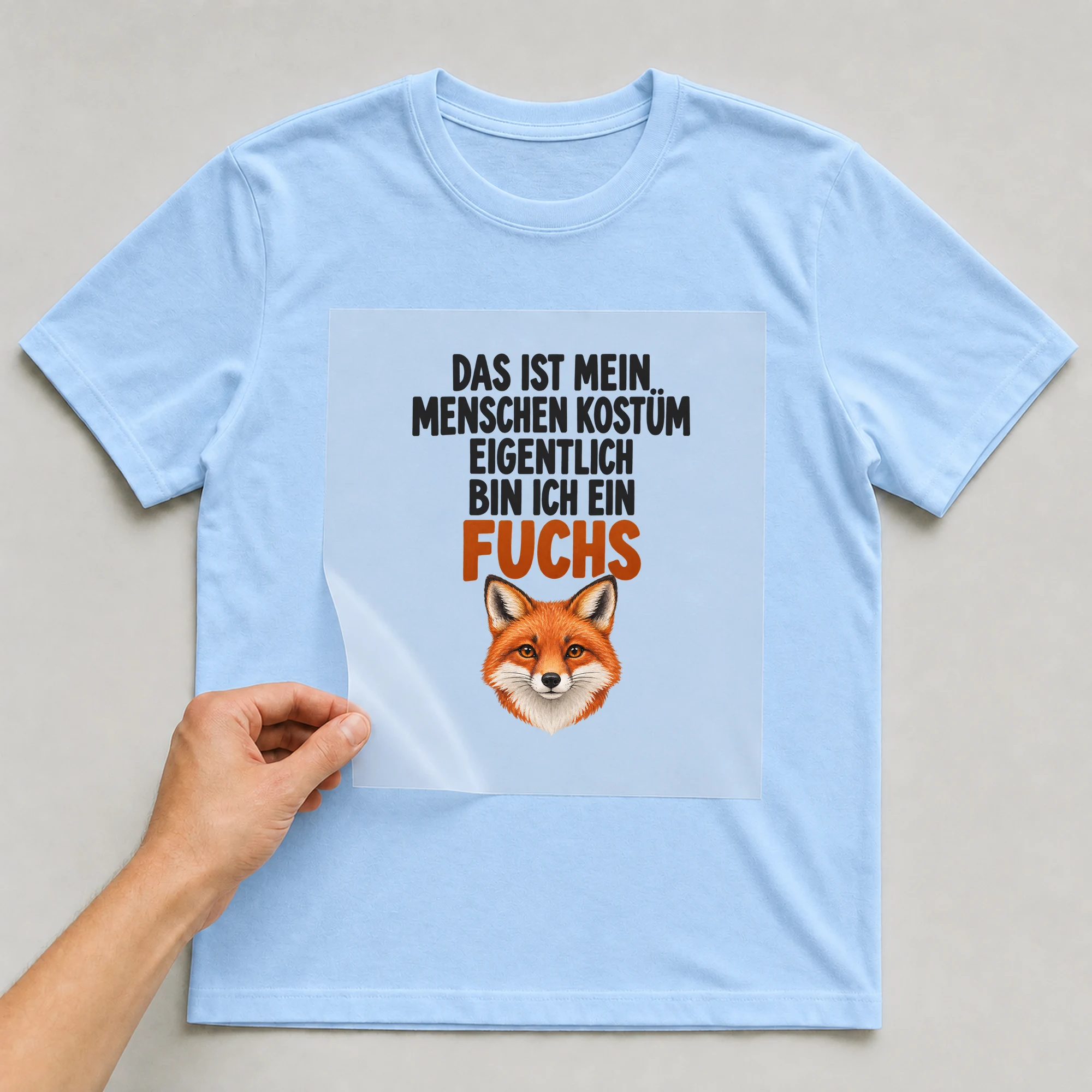Bügelbild „Das ist mein Menschen Kostüm eigentlich bin ich ein Fuchs“ auf babyblauem T-Shirt, Folie wird aufgelegt