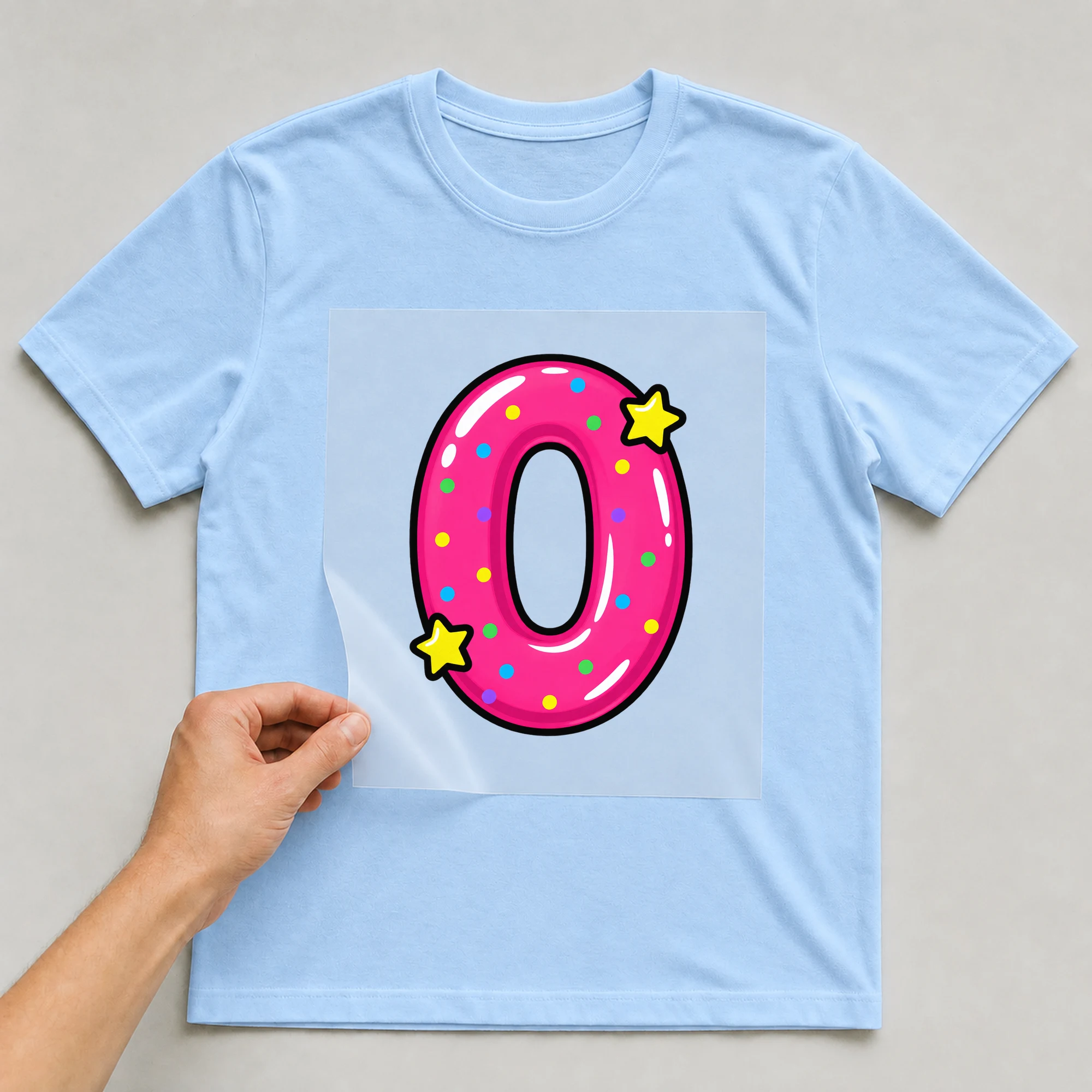 Bügelbild „Zahl 0 im Comic-Ballon-Stil“ auf babyblauem T-Shirt, Folie wird aufgelegt