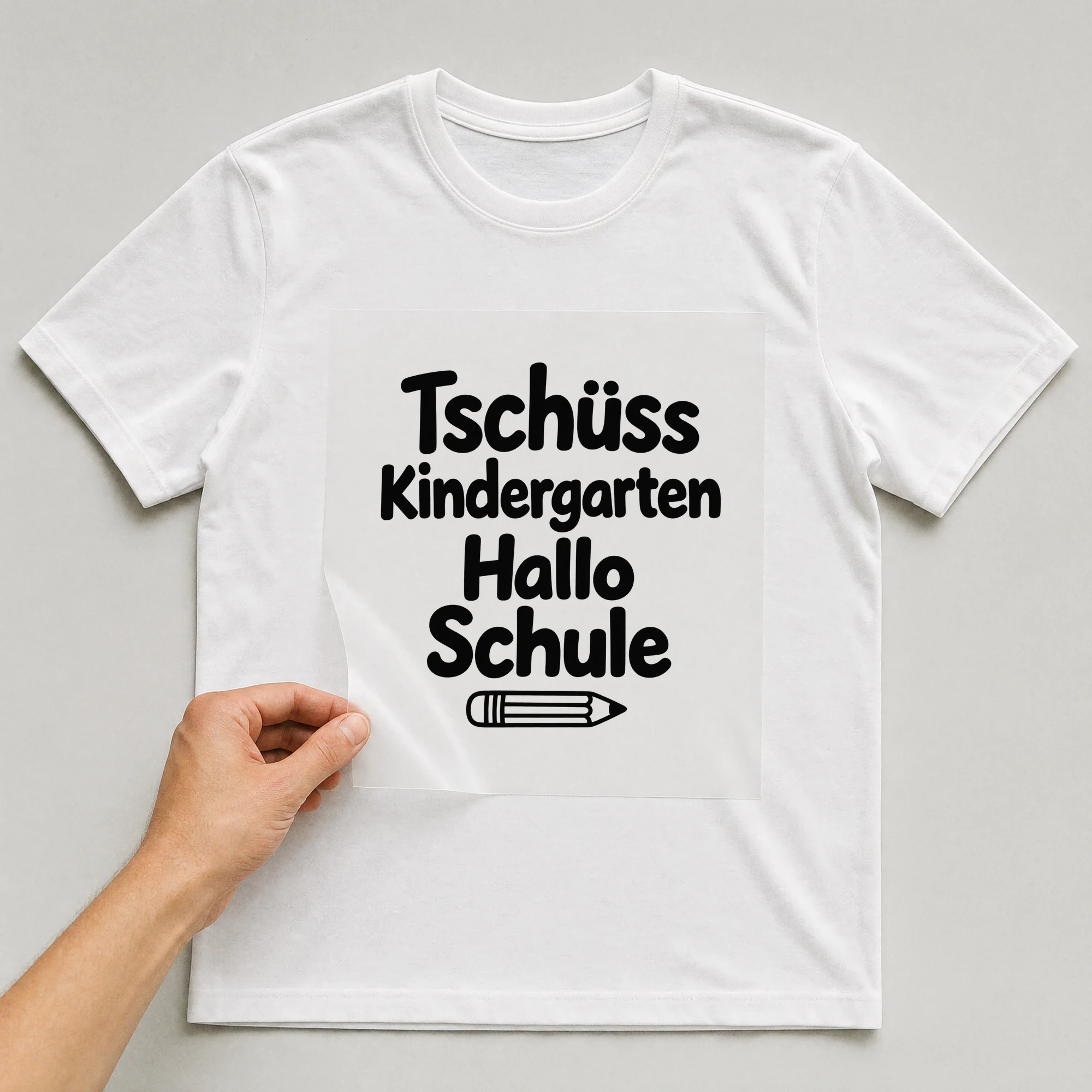 Bügelbild „Tschüss Kindergarten Hallo Schule“ auf weißem T-Shirt, Folie wird aufgelegt