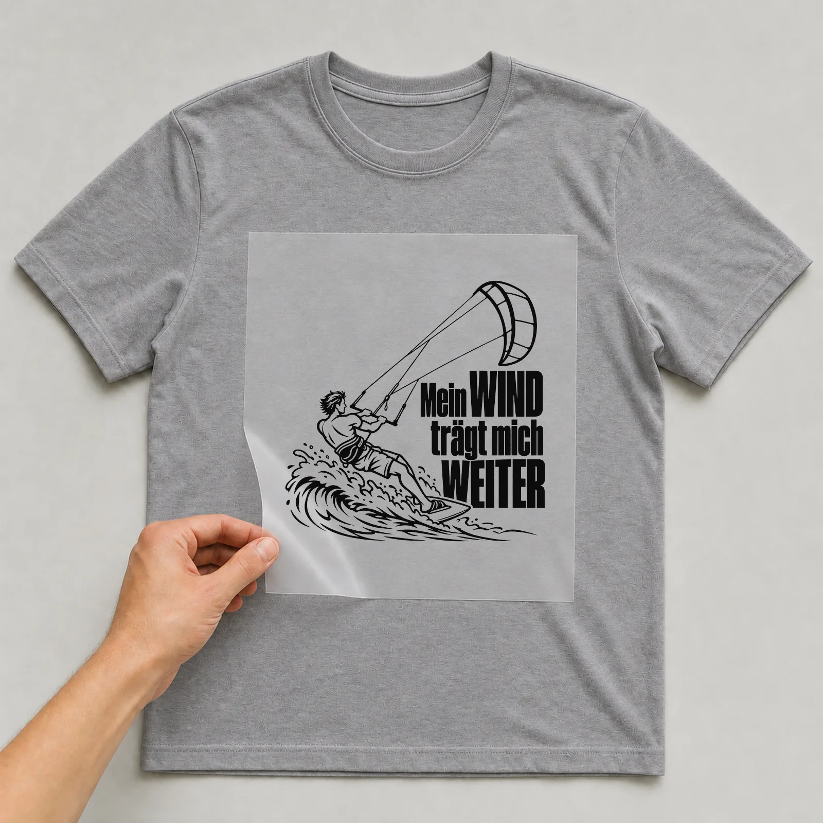 Bügelbild „Mein WIND trägt mich WEITER“ auf grauem T-Shirt, Folie wird aufgelegt