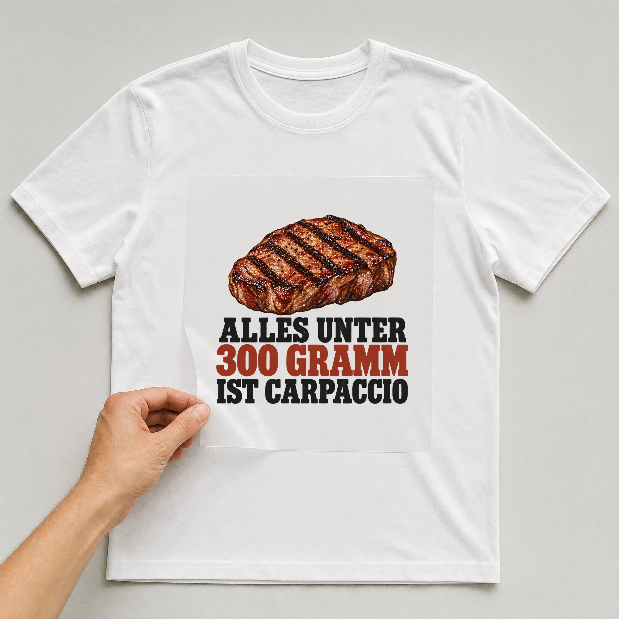 Bügelbild „Alles unter 300 Gramm ist Carpaccio“ auf weißem T-Shirt, Folie wird aufgelegt