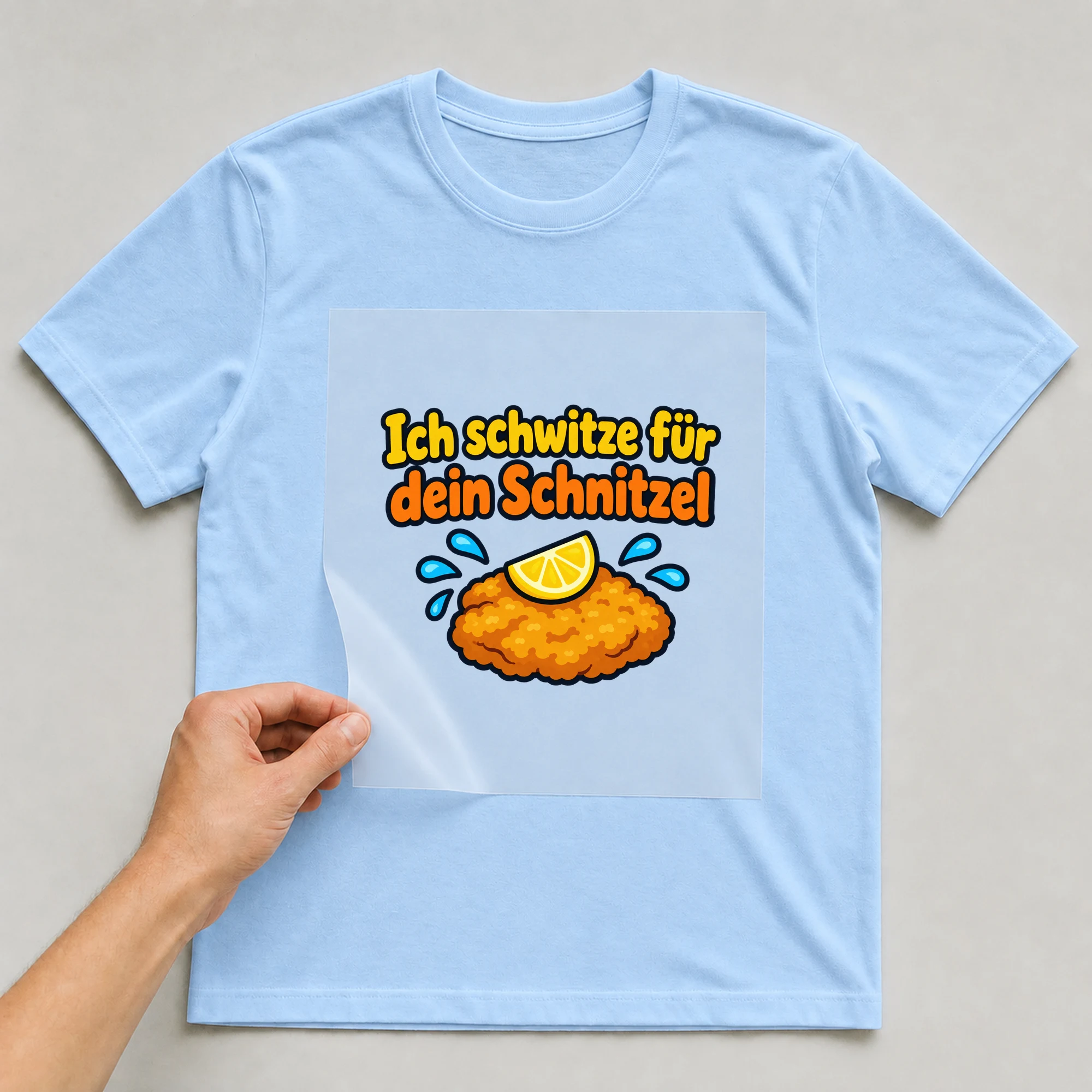 Bügelbild „Ich schwitze für dein Schnitzel“ auf babyblauem T-Shirt, Folie wird aufgelegt
