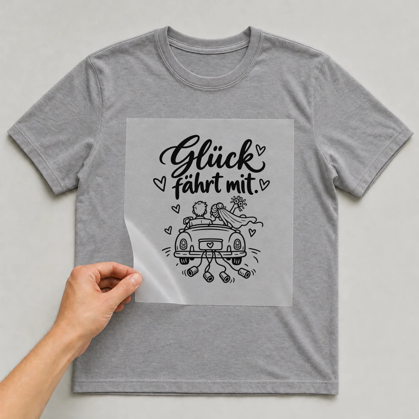 Bügelbild „Glück fährt mit“ auf grauem T-Shirt, Folie wird aufgelegt