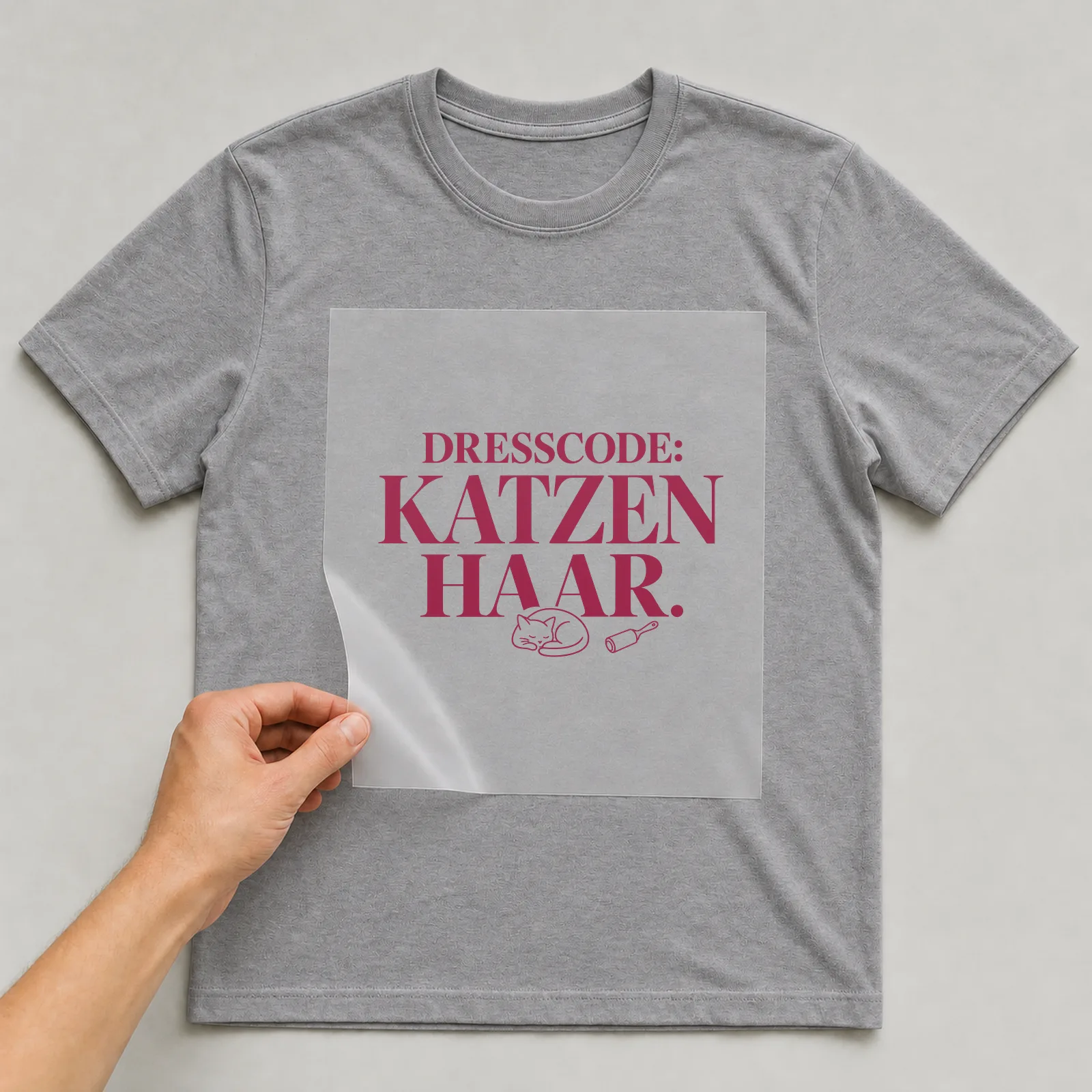 Bügelbild „Dresscode: Katzenhaar“ (Schrift Konturen) auf grauem T-Shirt, Folie wird aufgelegt