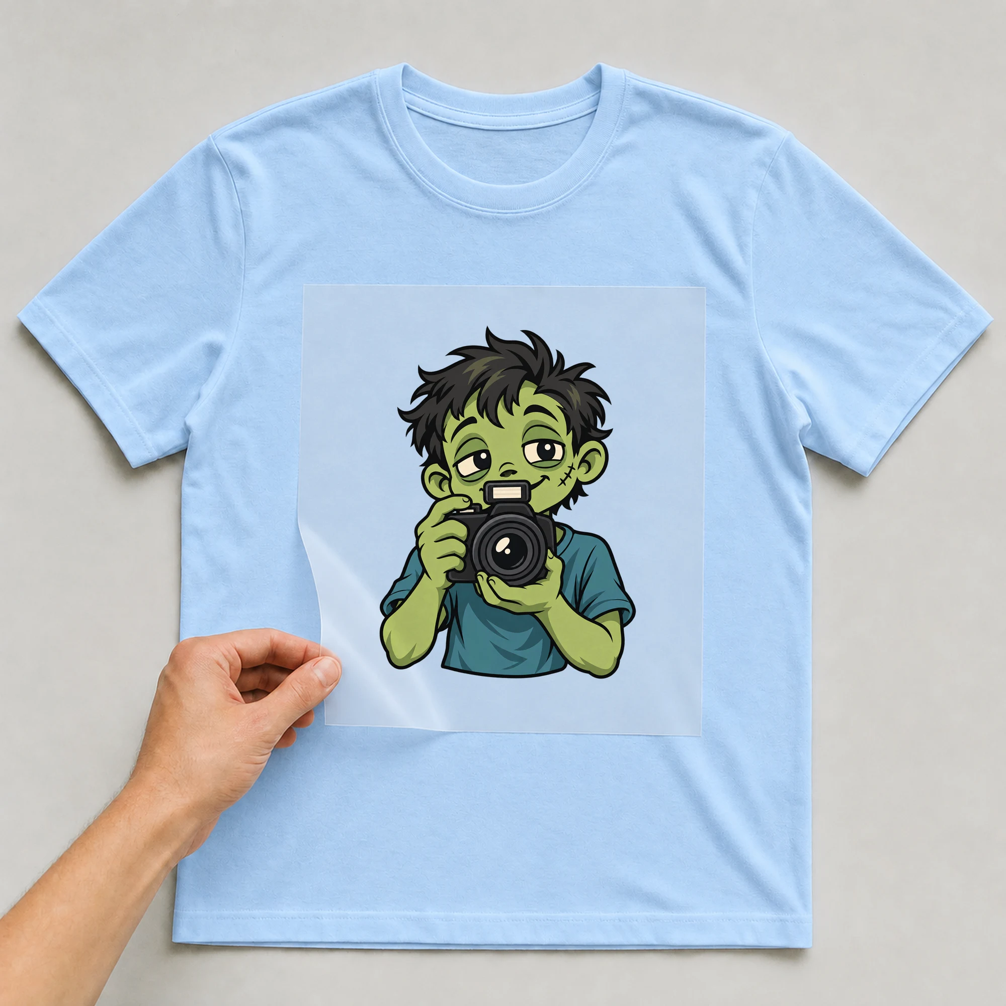 Bügelbild „Zombie Photographer“ auf babyblauem T-Shirt, Folie wird aufgelegt