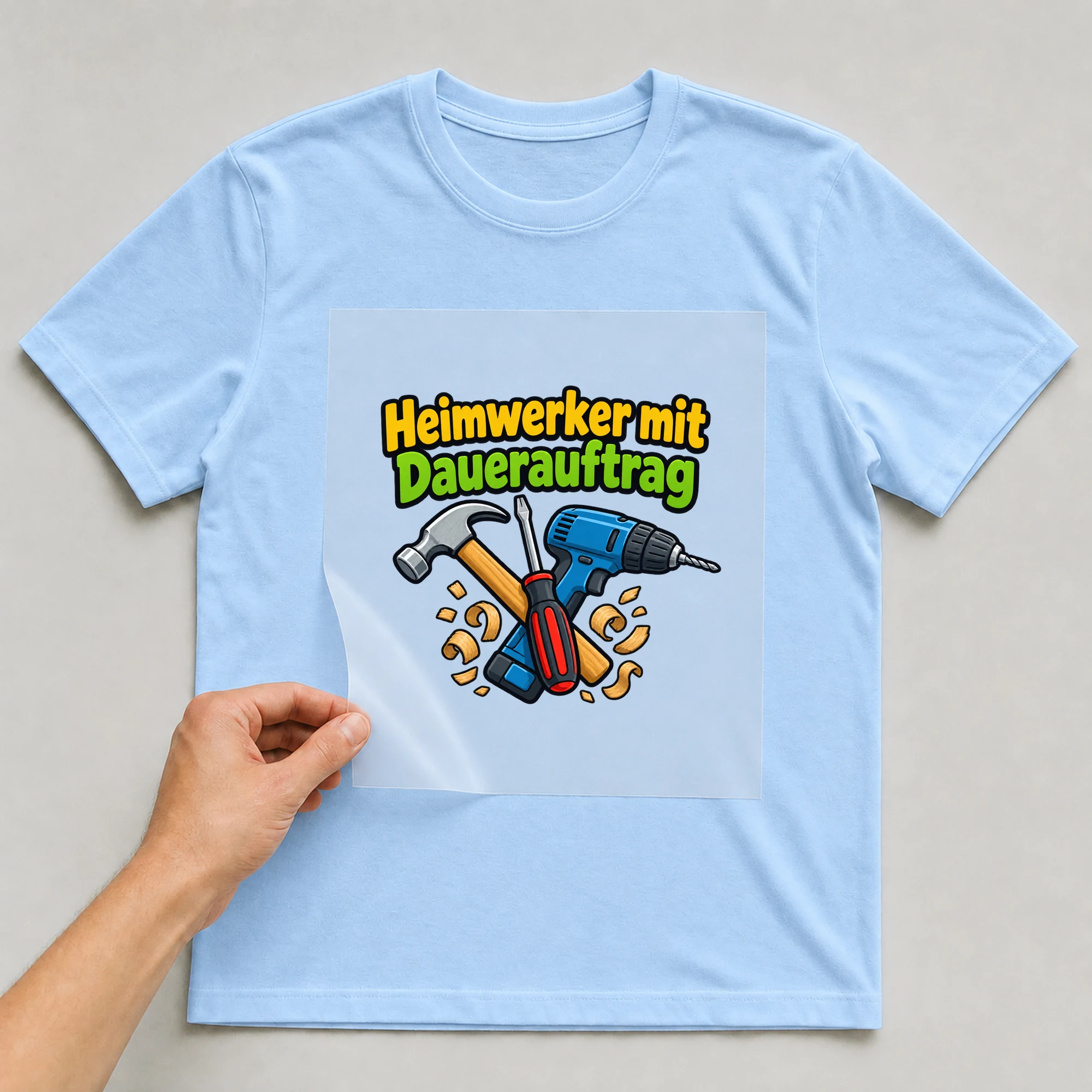 Bügelbild „Heimwerker mit Dauerauftrag“ auf babyblauem T-Shirt, Folie wird aufgelegt