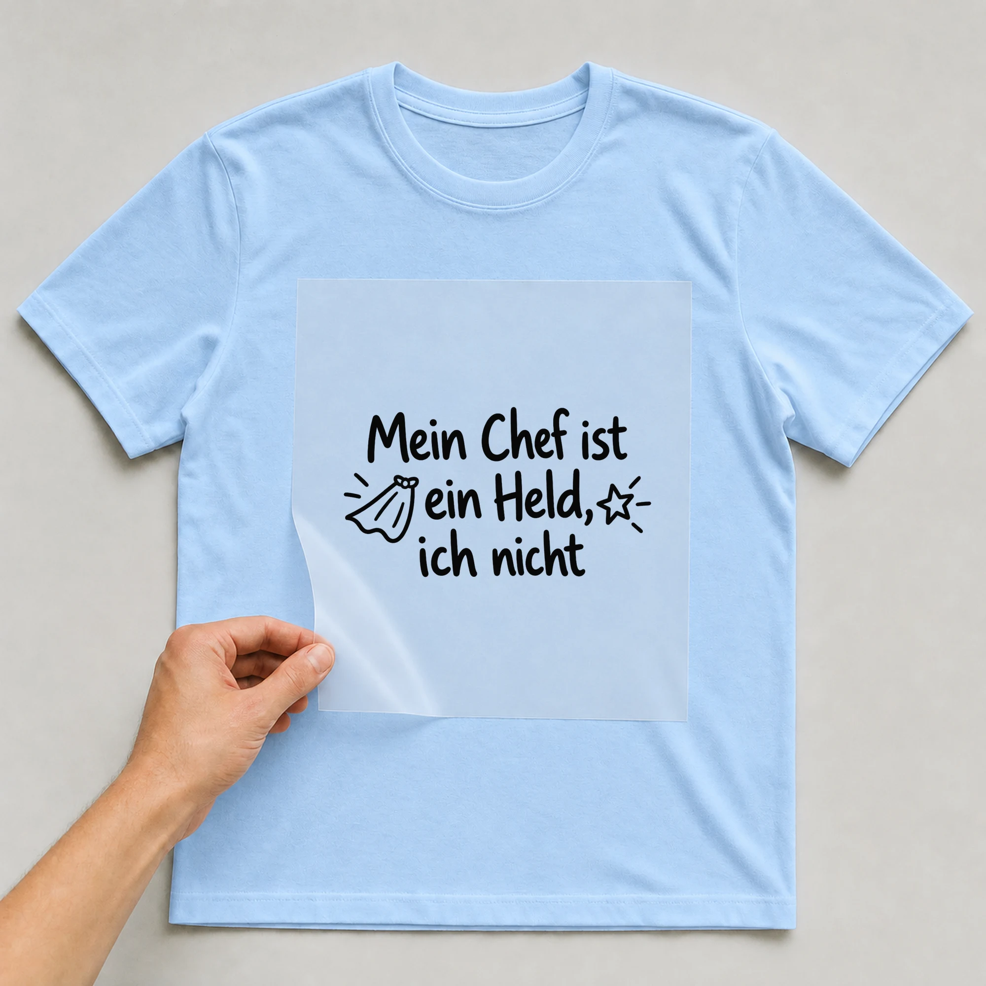 Bügelbild „Mein Chef ist ein Held, ich nicht“ auf babyblauem T-Shirt, Folie wird aufgelegt