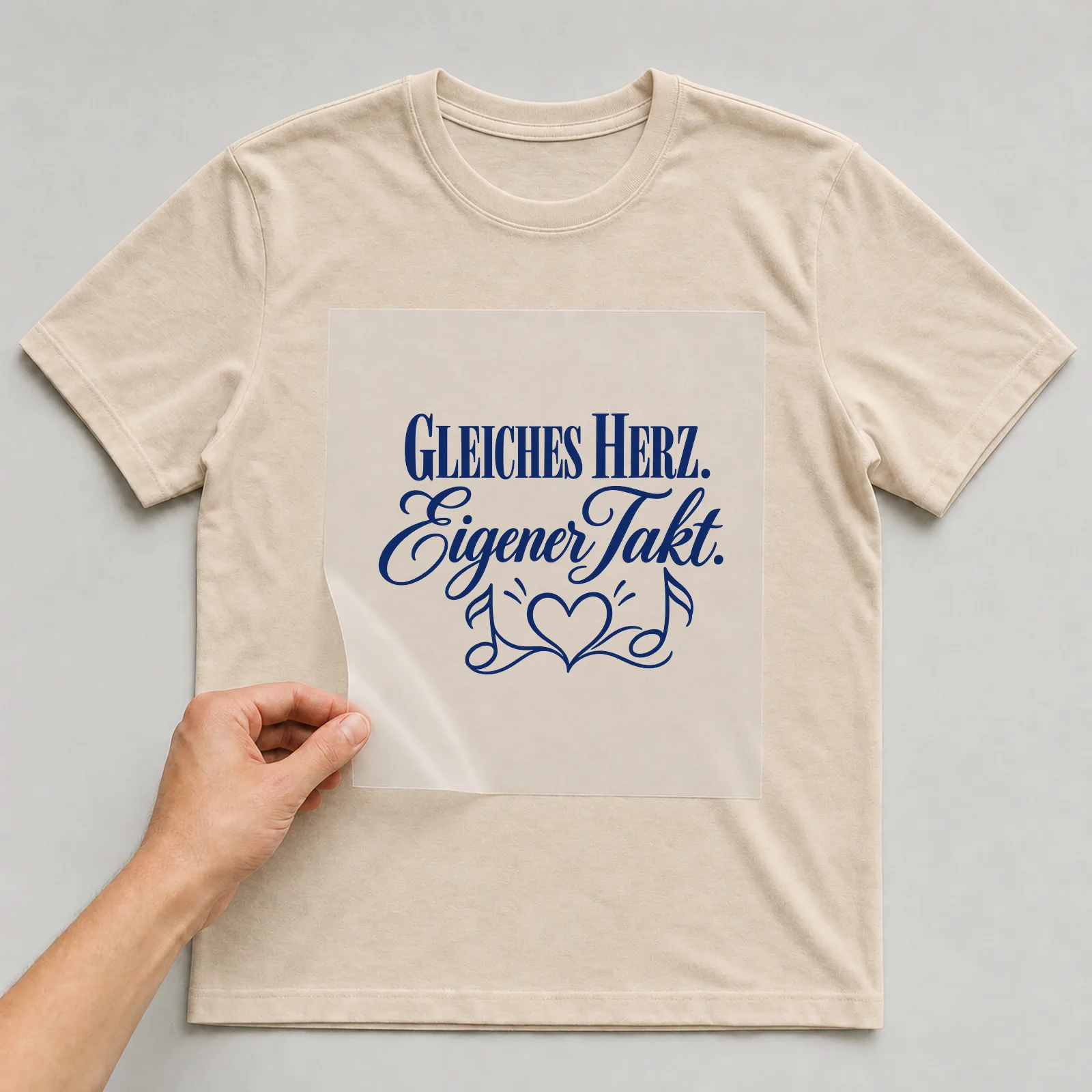 Bügelbild „Gleiches Herz. Eigener Takt.“ auf beigem T-Shirt, Folie wird aufgelegt