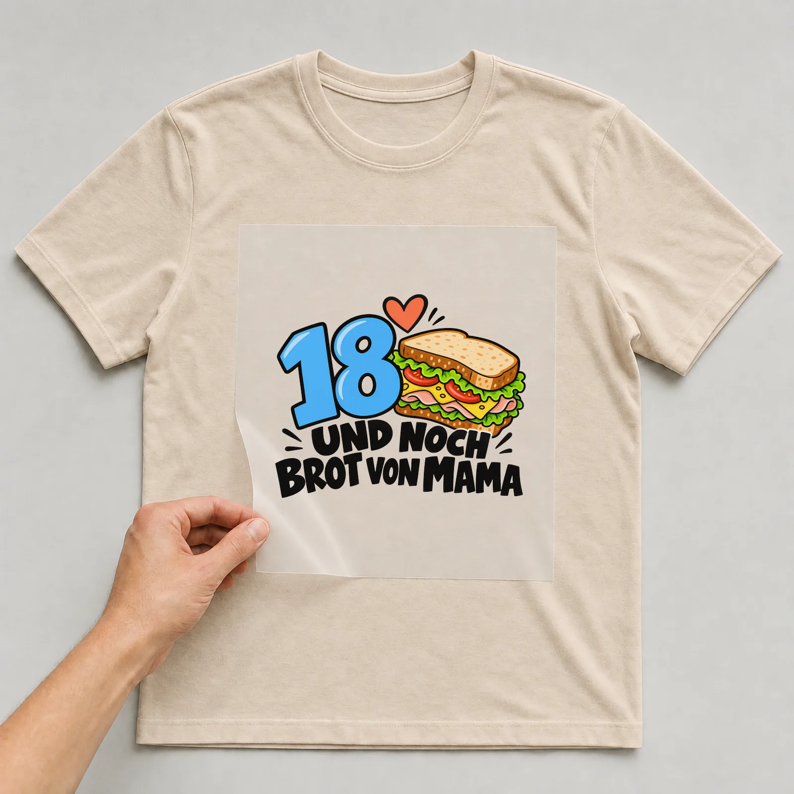 Bügelbild „18 Und noch Brot von Mama“ auf beigem T-Shirt, Folie wird aufgelegt