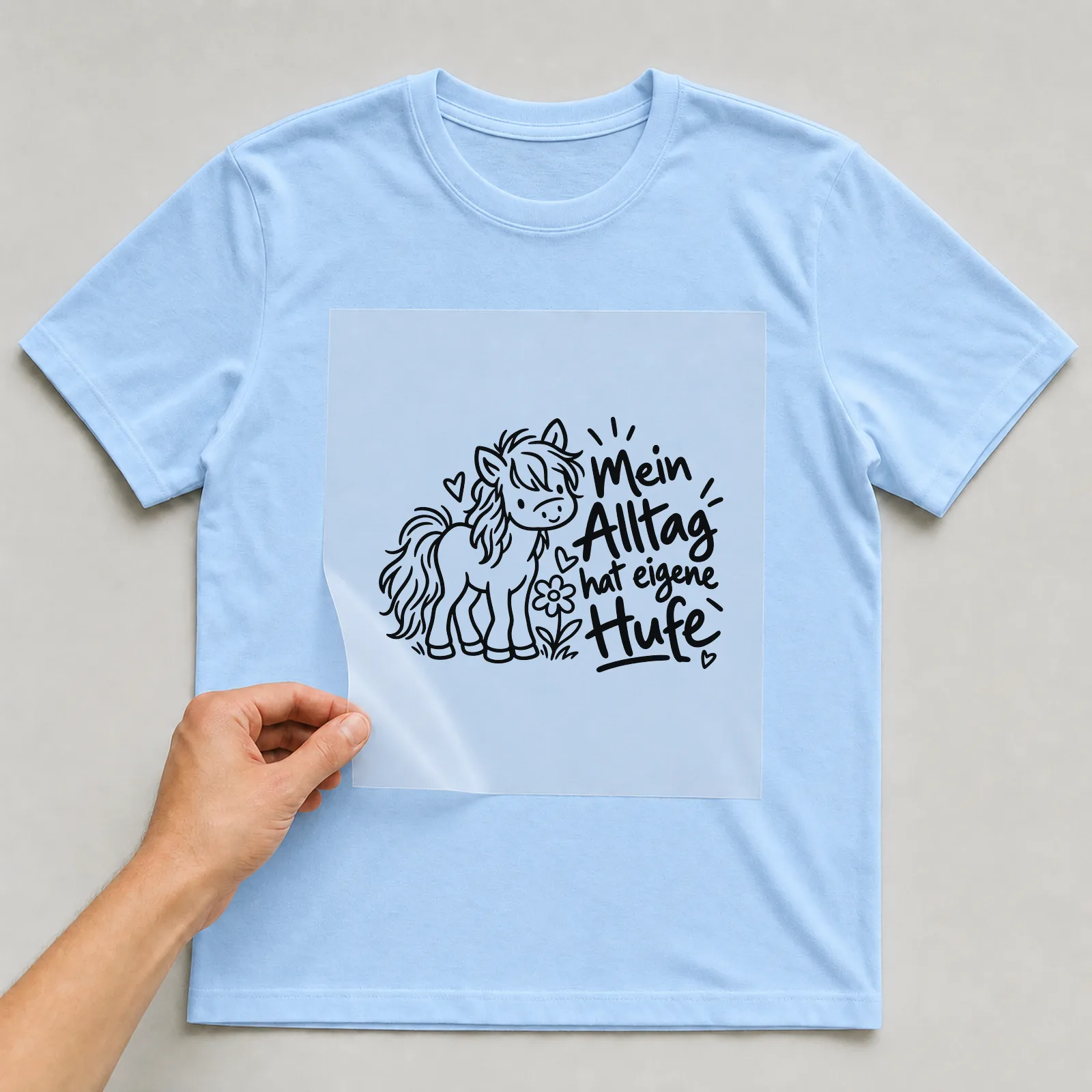 Bügelbild „Mein Alltag hat eigene Hufe“ auf hellblauem T-Shirt, Folie wird aufgelegt