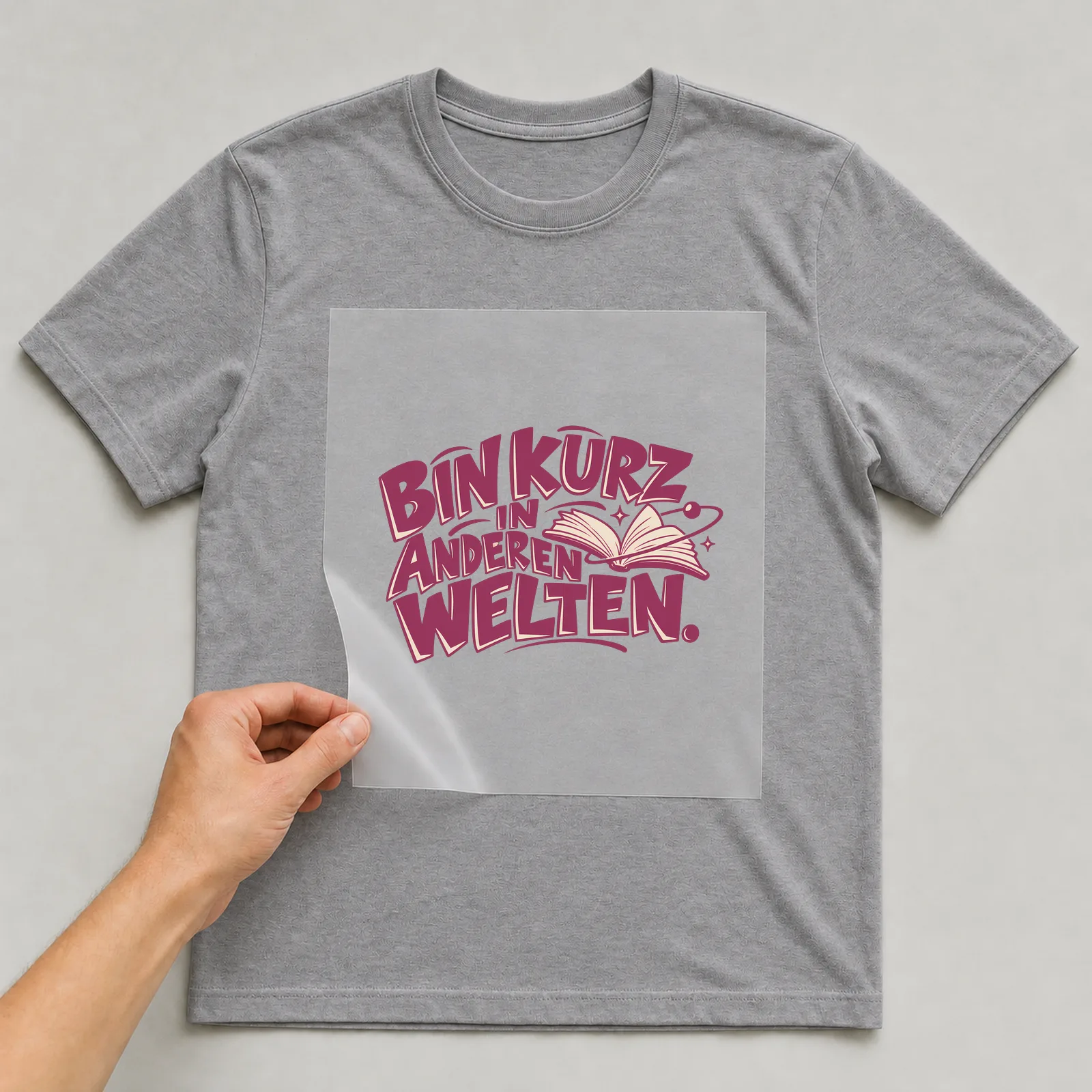 Bügelbild „Bin kurz in anderen Welten“ auf grauem T-Shirt, Folie wird aufgelegt