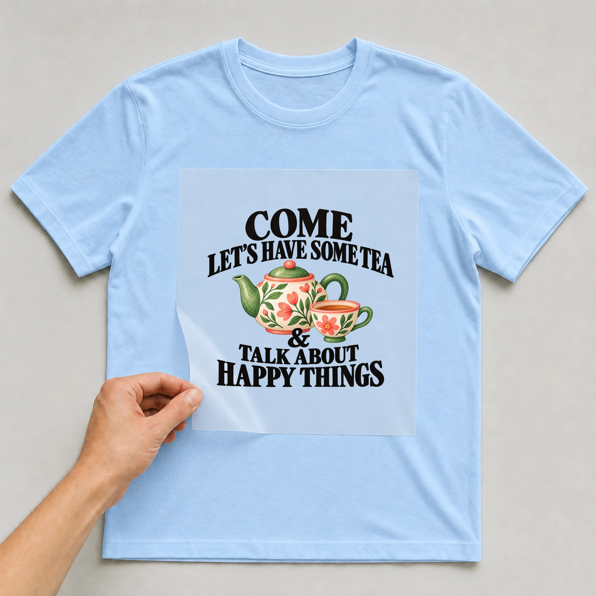 Bügelbild „Come Let's Have Some Tea & Talk About Happy Things“ auf babyblauem T-Shirt, Folie wird aufgelegt