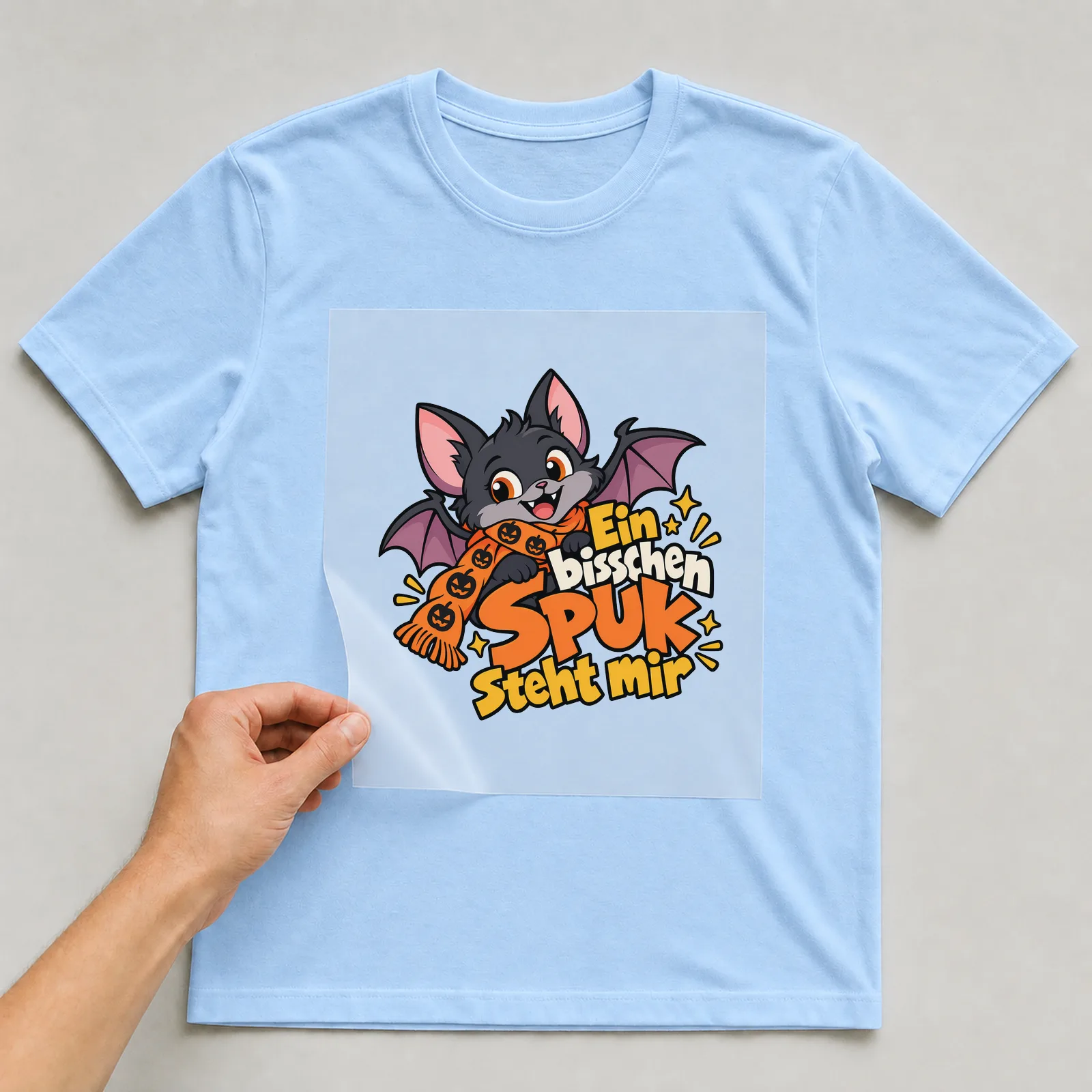 Bügelbild „Ein bisschen Spuk steht mir“ auf hellblauem T-Shirt, Folie wird aufgelegt