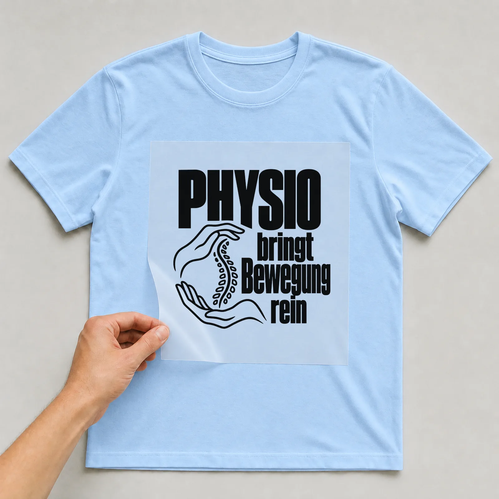 Bügelbild „Physio bringt Bewegung rein“ auf hellblauem T-Shirt, Folie wird aufgelegt