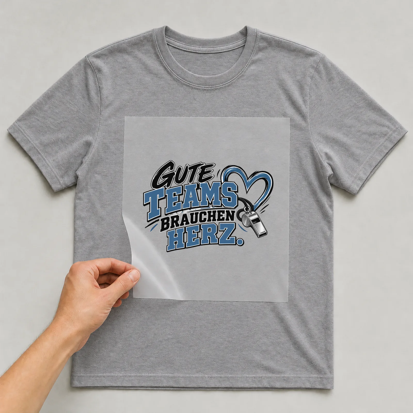 Bügelbild „Gute Teams brauchen Herz“ auf grauem T-Shirt, Folie wird aufgelegt