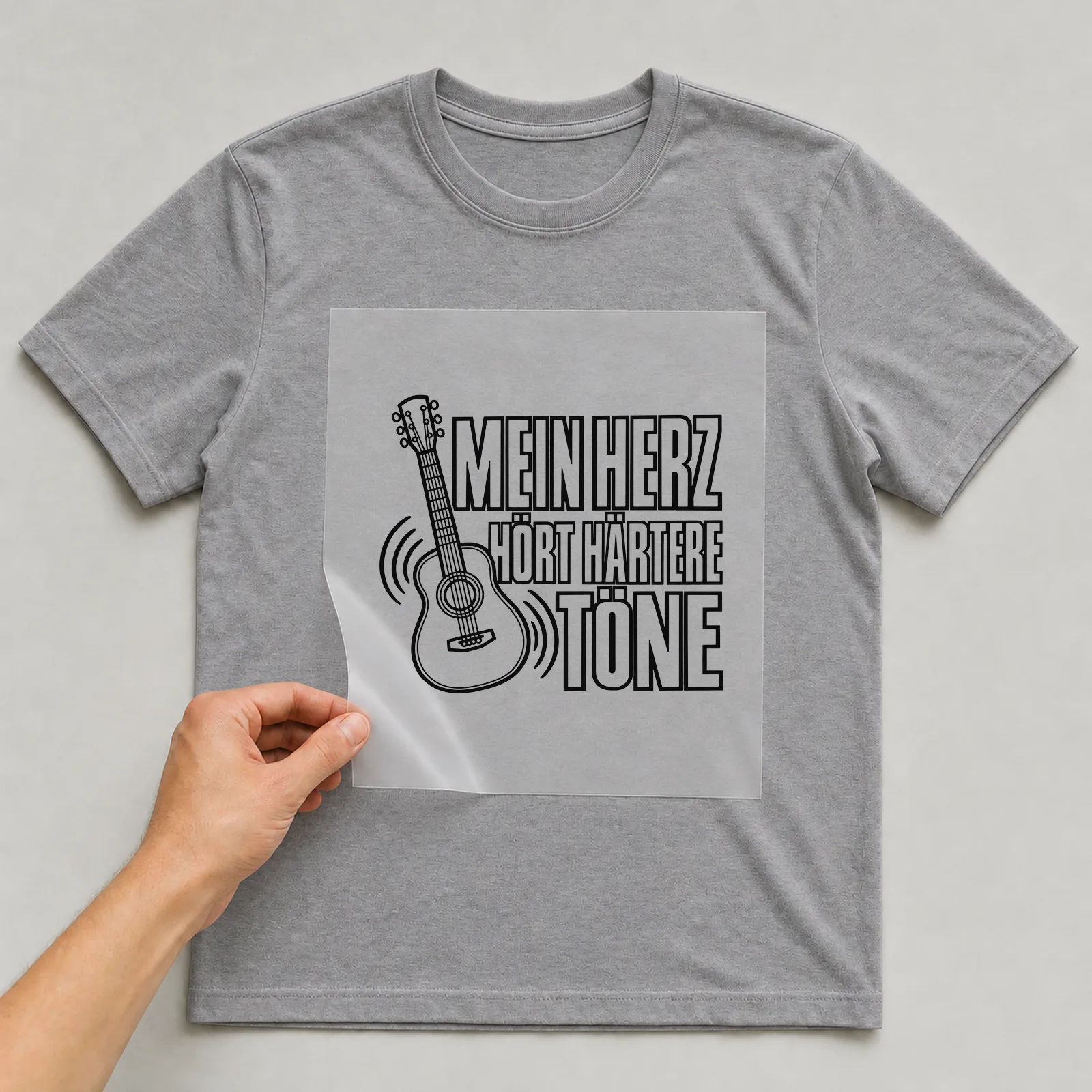 Bügelbild „Mein Herz hört härtere töne“ auf grauem T-Shirt, Folie wird aufgelegt