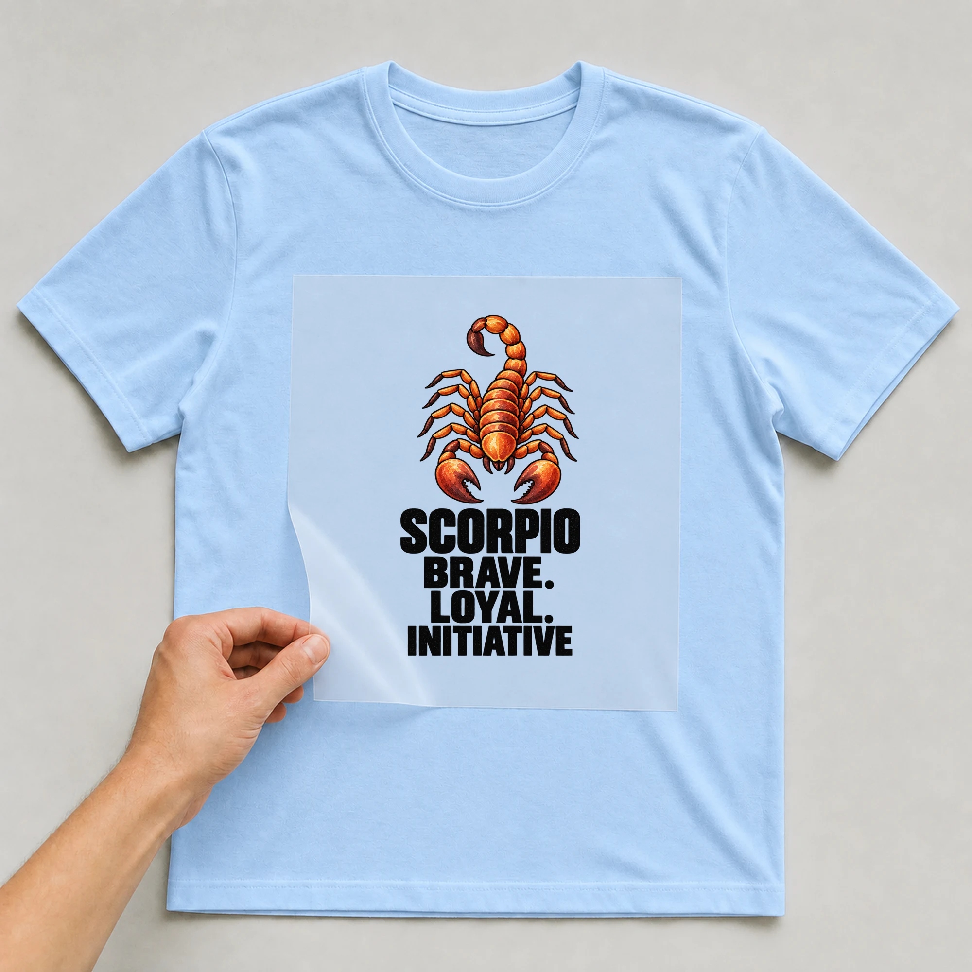 Bügelbild „Scorpio Brave. Loyal. Initiative“ auf babyblauem T-Shirt, Folie wird aufgelegt
