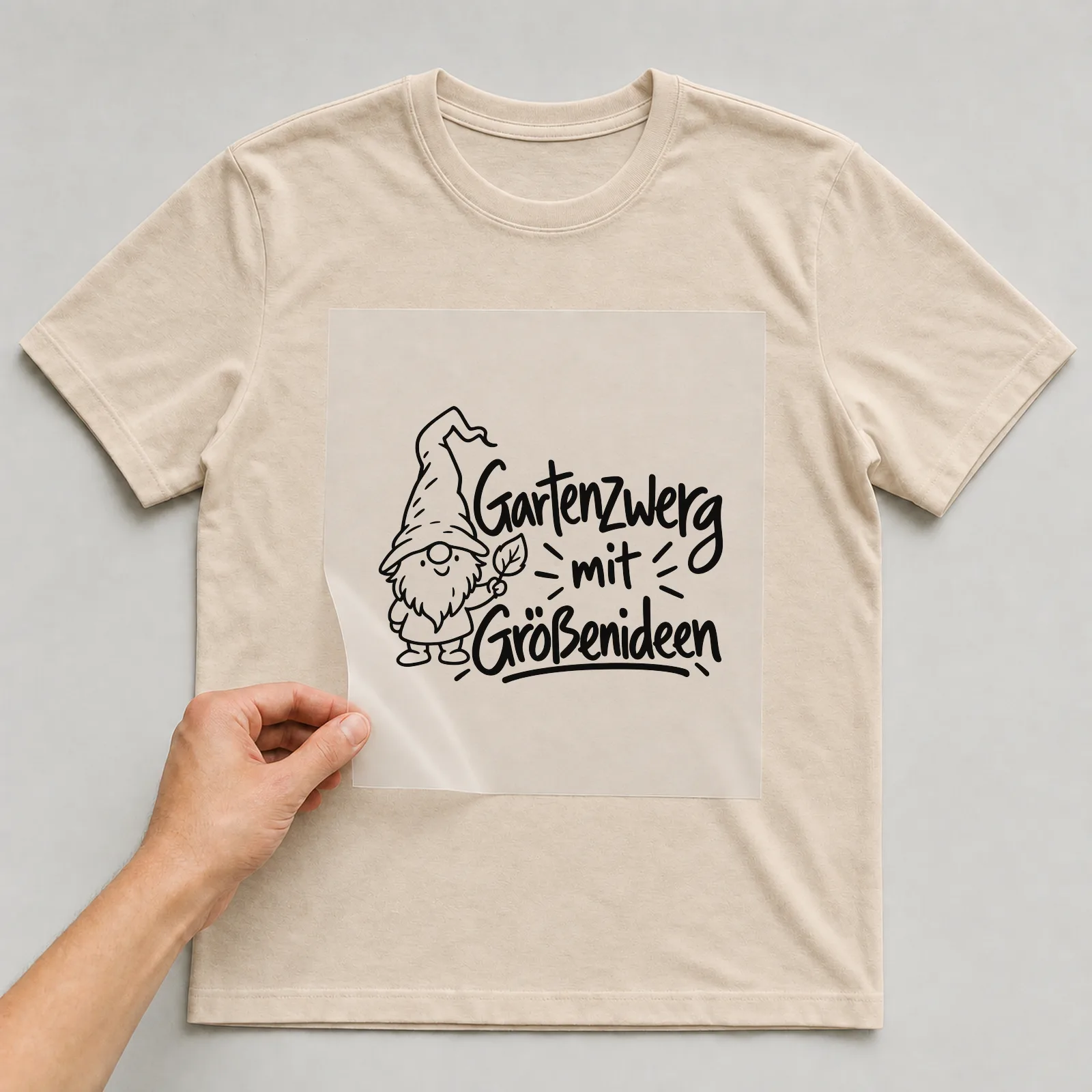 Bügelbild „Gartenzwerg mit Größenideen“ auf beigem T-Shirt, Folie wird aufgelegt