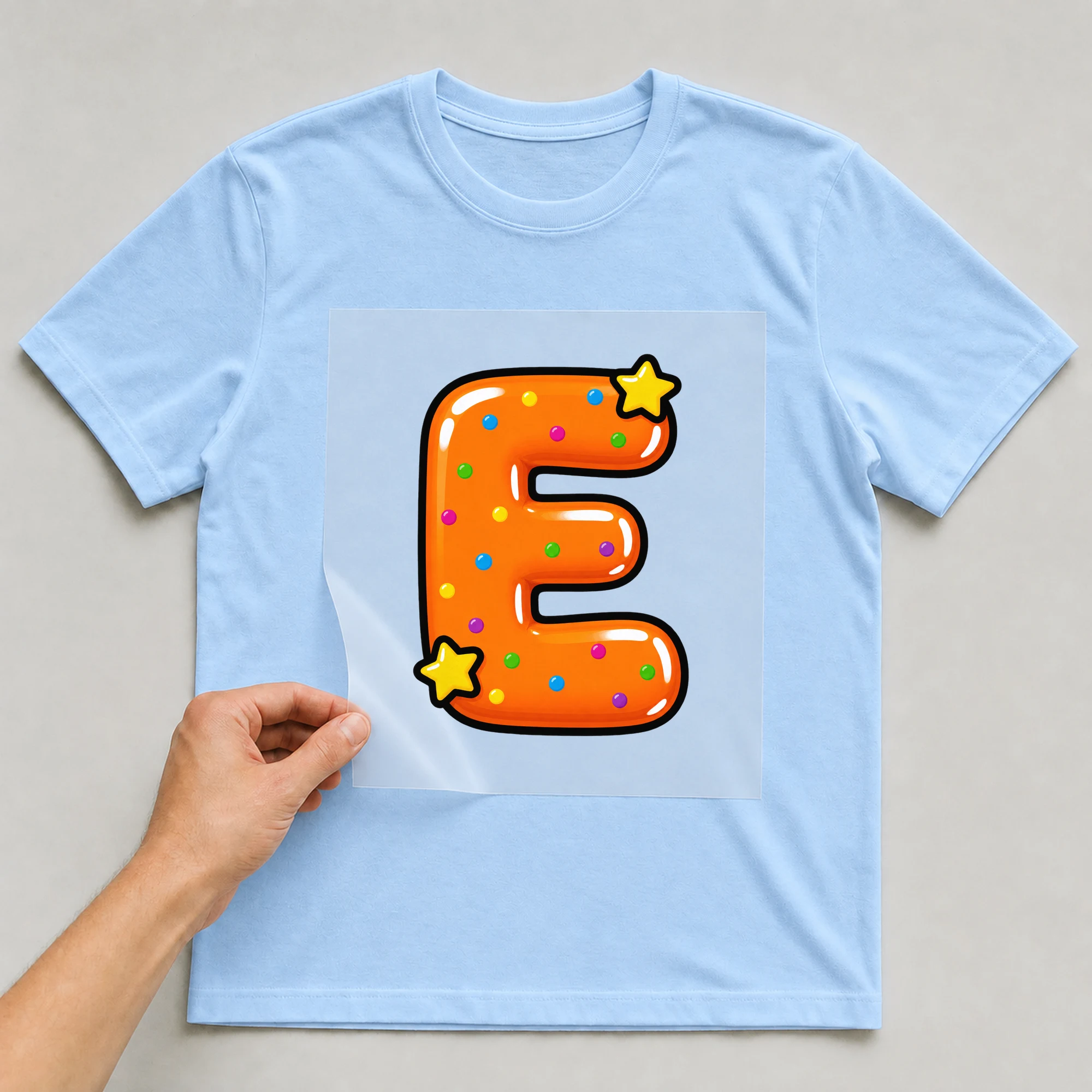 Bügelbild „Buchstabe E im Comic-Ballon-Stil“ auf babyblauem T-Shirt, Folie wird aufgelegt