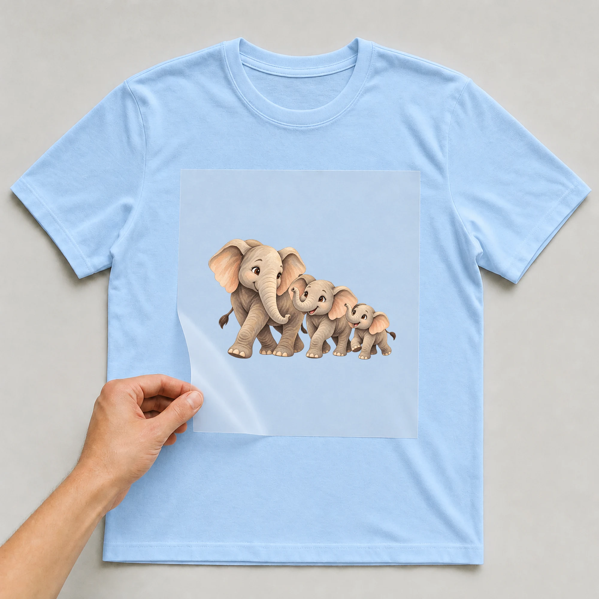 Bügelbild „Elefant Familie“ auf babyblauem T-Shirt, Folie wird aufgelegt