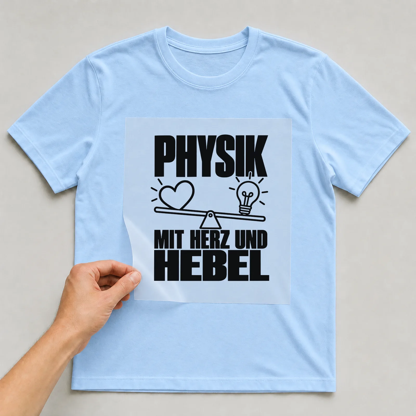 Bügelbild „Physik mit Herz und hebel“ auf hellblauem T-Shirt, Folie wird aufgelegt