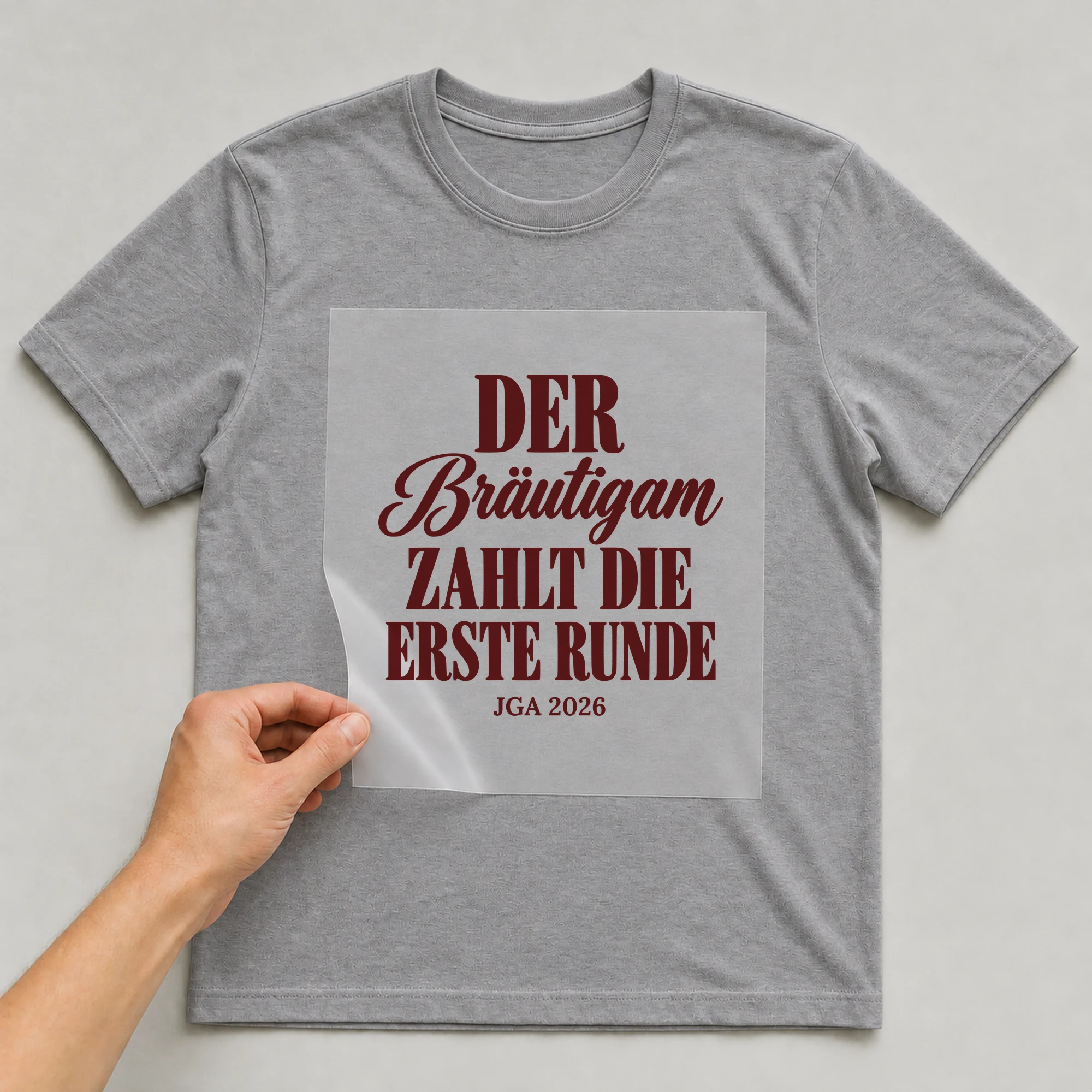 Bügelbild Der Bräutigam zahlt die erste Runde mit Jahr auf grauem T-Shirt, Folie wird aufgelegt