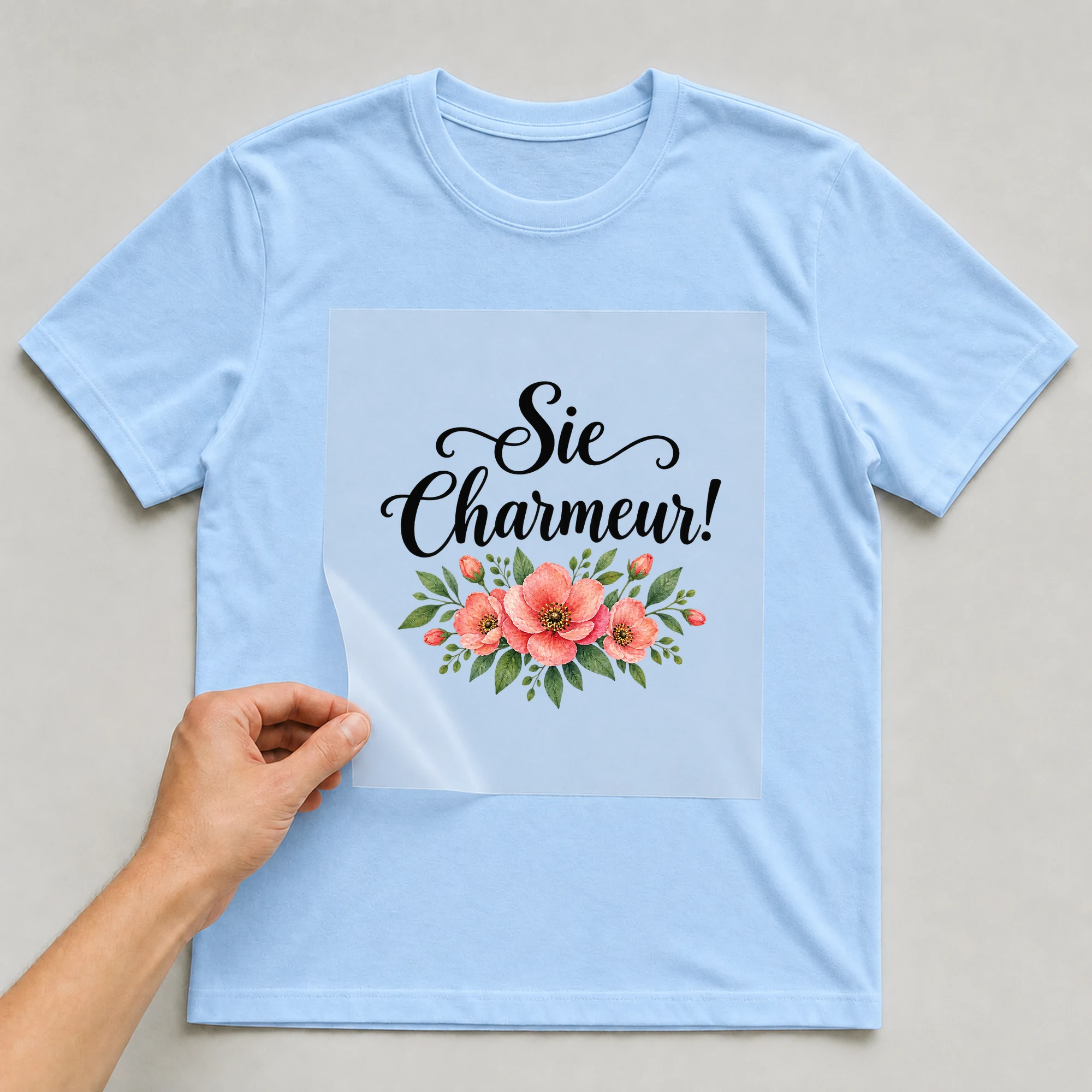 Bügelbild „Sie Charmeur!“ auf babyblauem T-Shirt, Folie wird aufgelegt