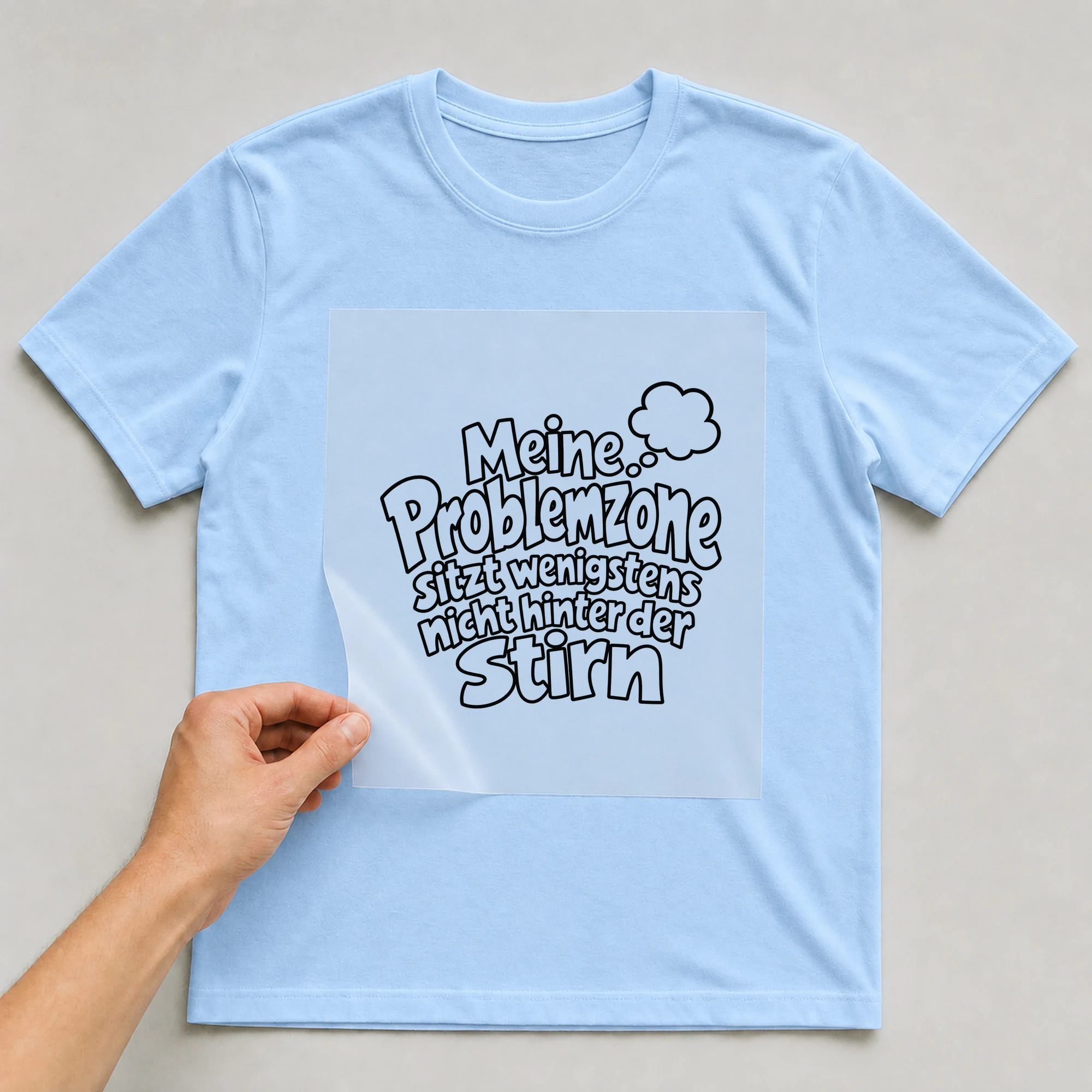 Bügelbild „Meine Problemzone sitzt wenigstens nicht hinter der Stirn“ auf babyblauem T-Shirt, Folie wird aufgelegt