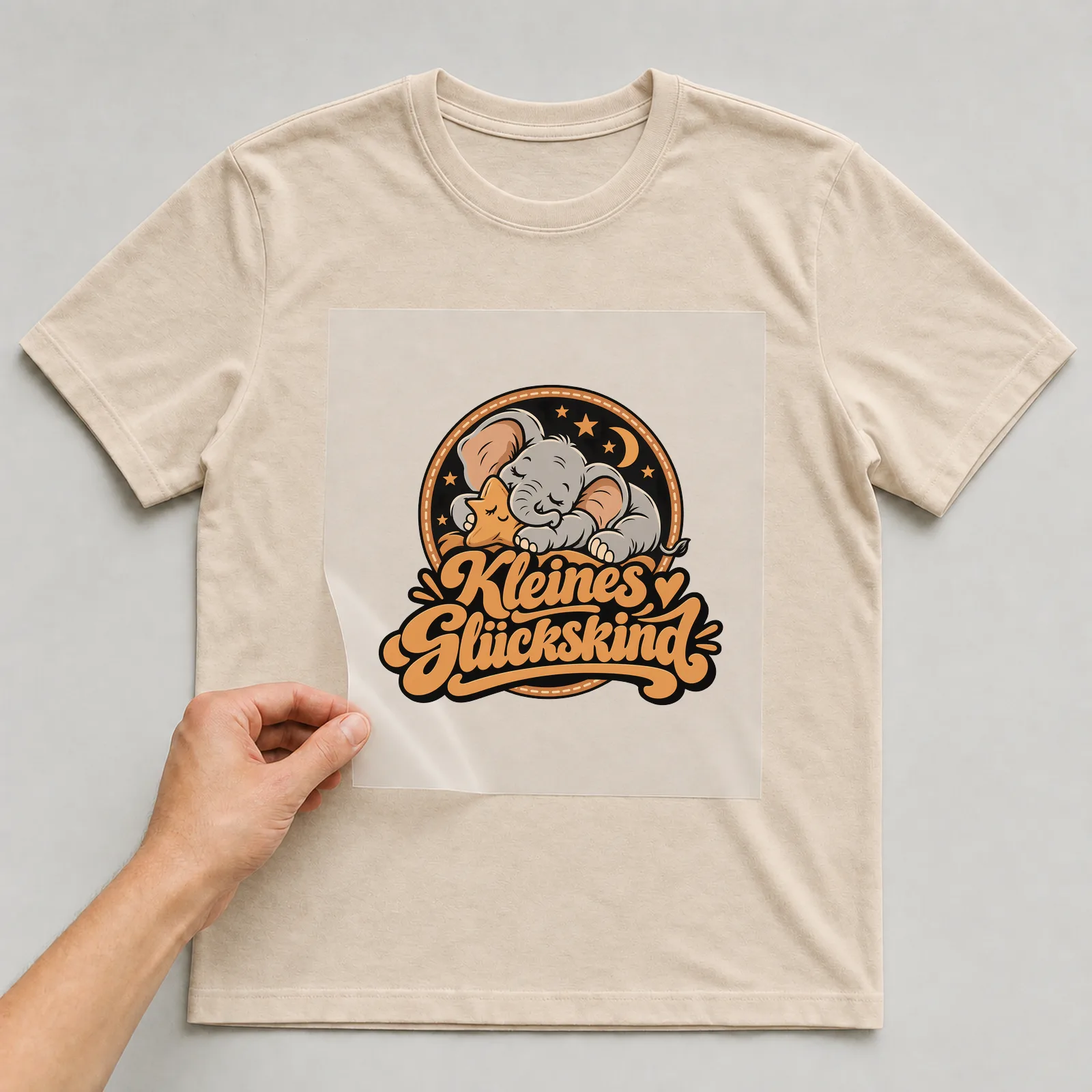 Bügelbild „Kleines Glückskind“ auf beigem T-Shirt, Folie wird aufgelegt
