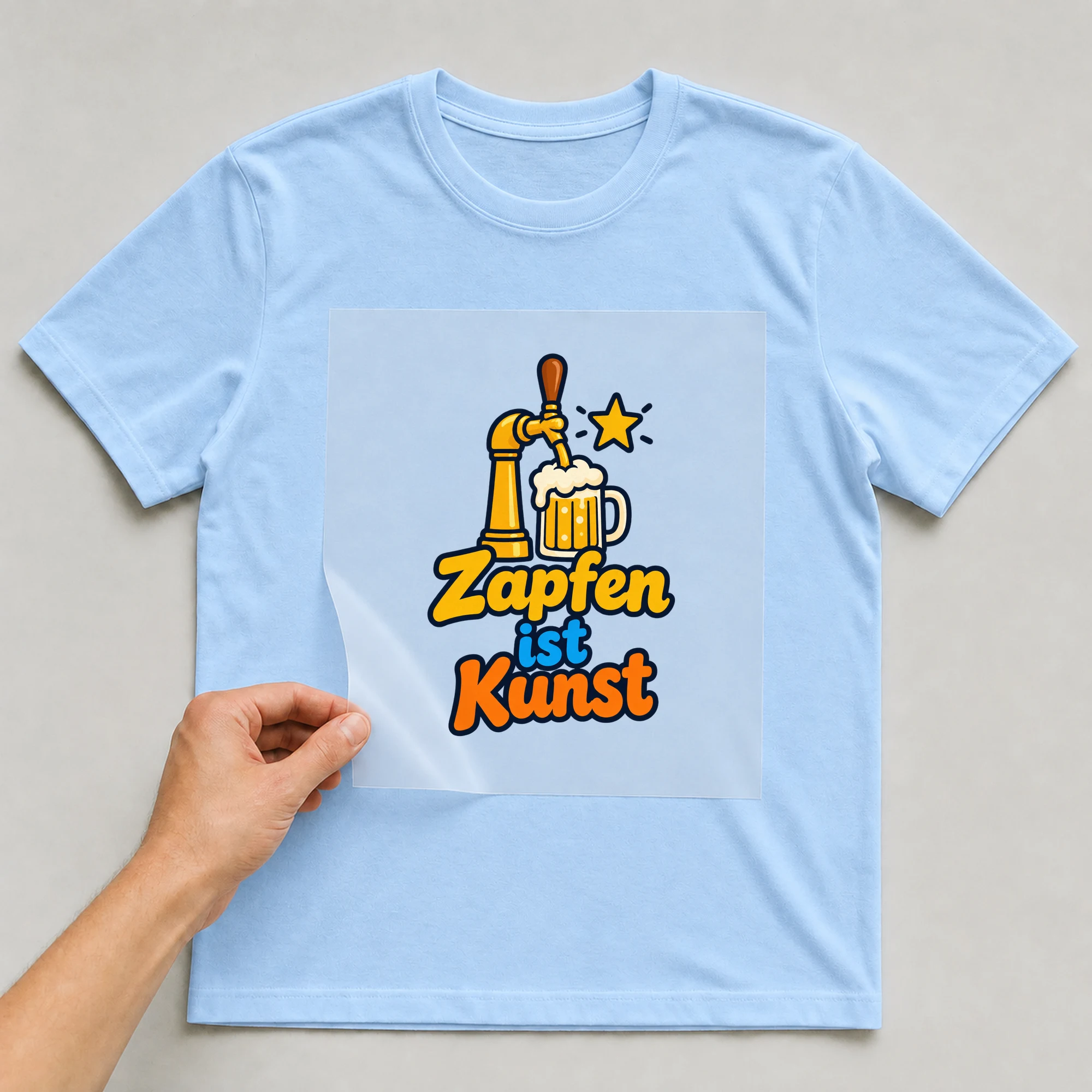 Bügelbild „Zapfen ist Kunst“ auf babyblauem T-Shirt, Folie wird aufgelegt