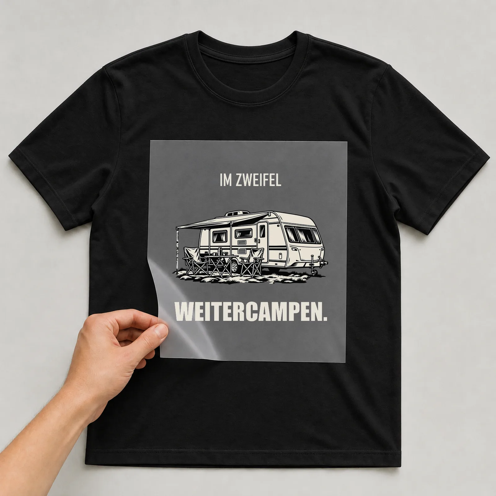 Bügelbild „Im Zweifel Weitercampen“ auf schwarzem T-Shirt, Folie wird aufgelegt