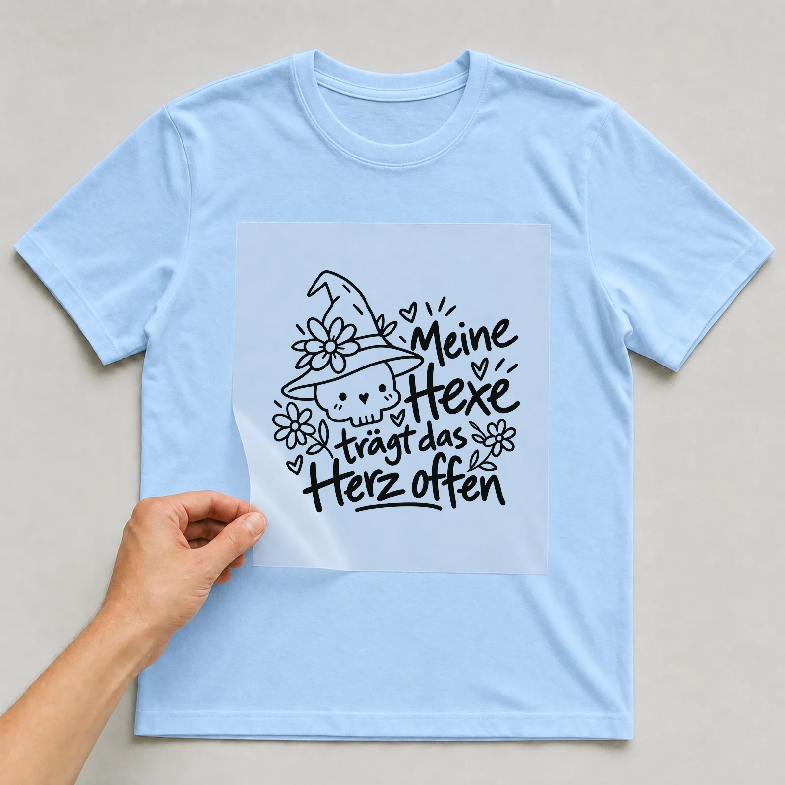 Bügelbild „Meine Hexe trägt das Herz offen“ auf hellblauem T-Shirt, Folie wird aufgelegt