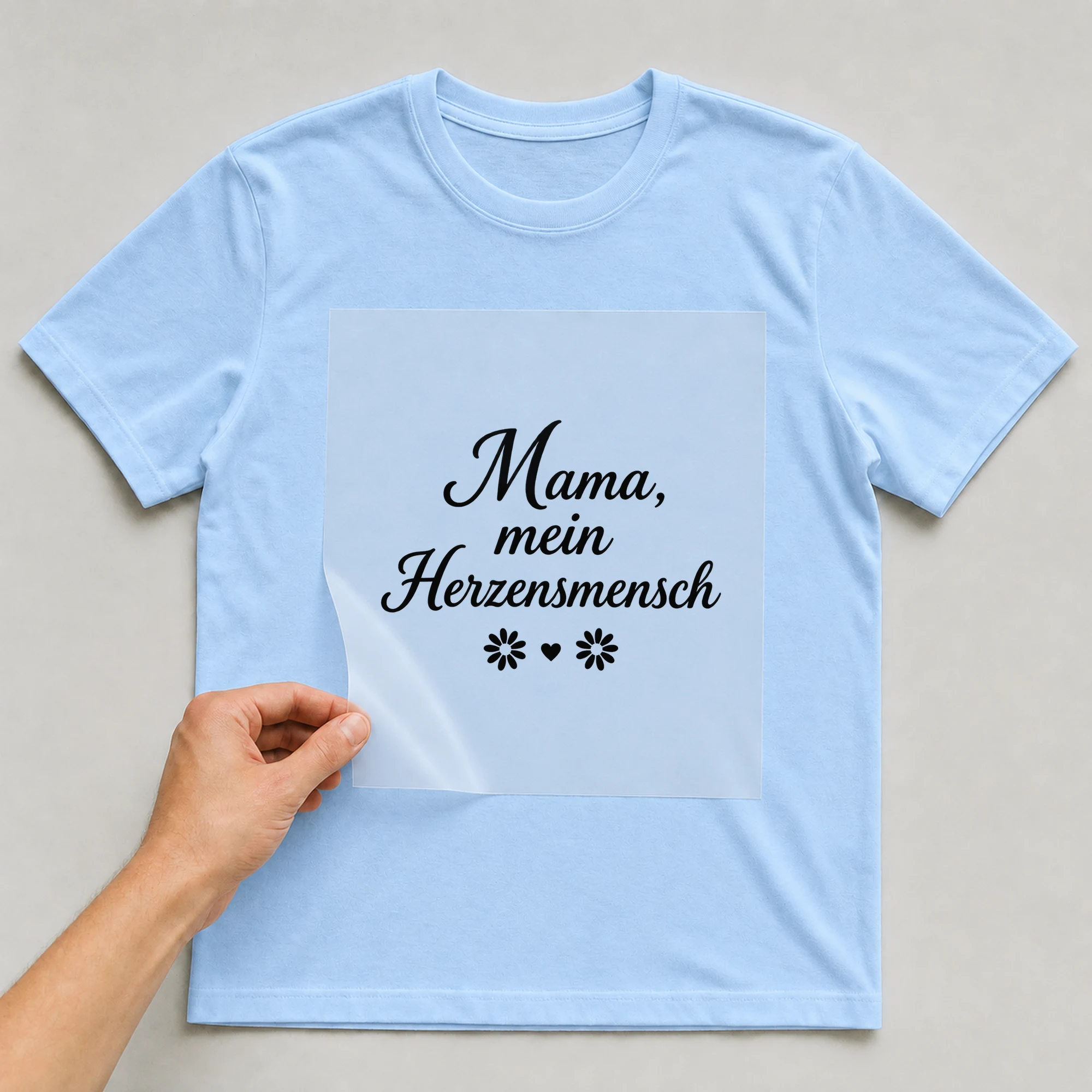 Bügelbild „Mama, mein Herzensmensch“ auf hellblauem T-Shirt, Folie wird aufgelegt