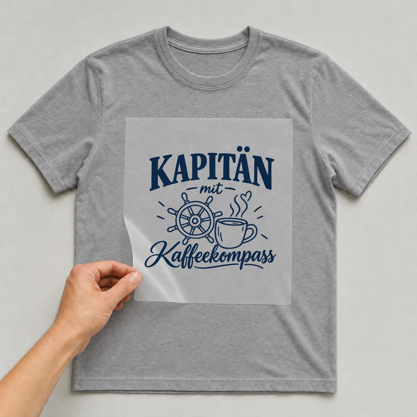 Bügelbild „Kapitän mit Kaffeekompass“ auf grauem T-Shirt, Folie wird aufgelegt