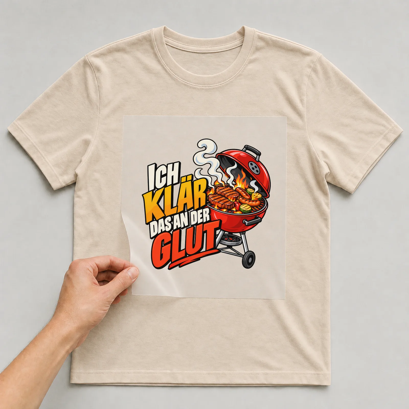 Bügelbild „Ich klär das an der Glut“ auf beigem T-Shirt, Folie wird aufgelegt