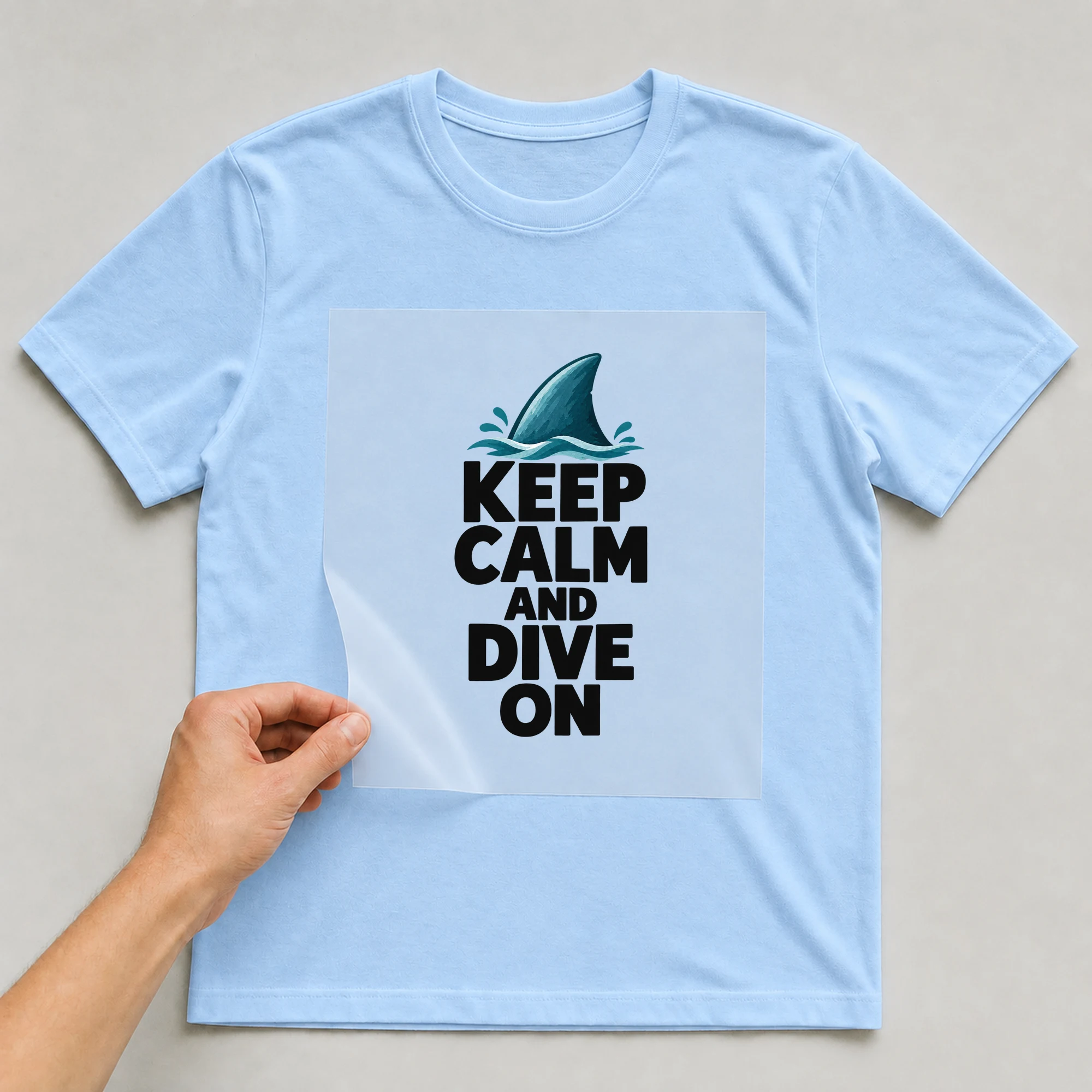 Bügelbild „KEEP CALM AND DIVE ON“ auf babyblauem T-Shirt, Folie wird aufgelegt