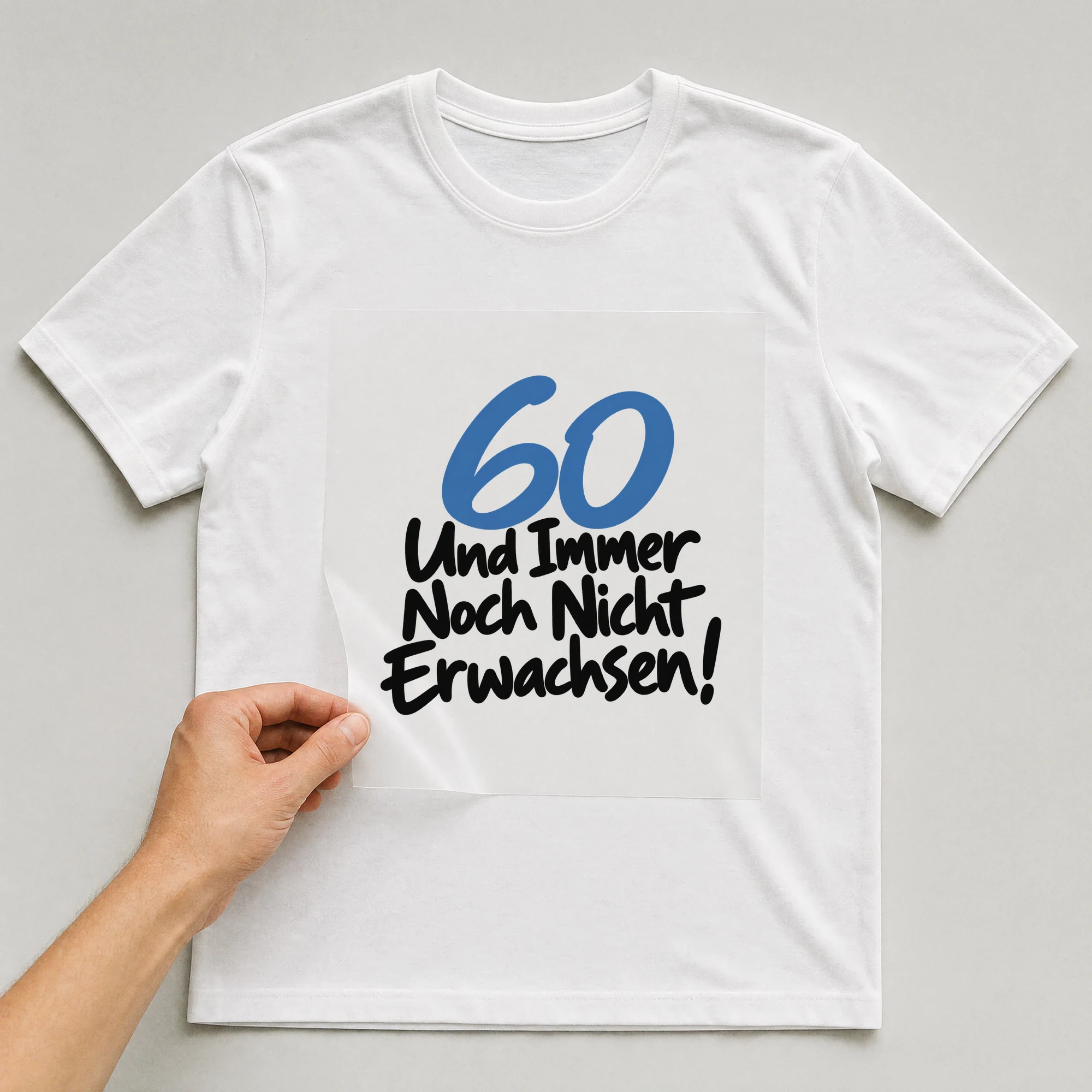 Bügelbild „60 Und immer noch nicht erwachsen!“ auf weißem T-Shirt, Folie wird aufgelegt