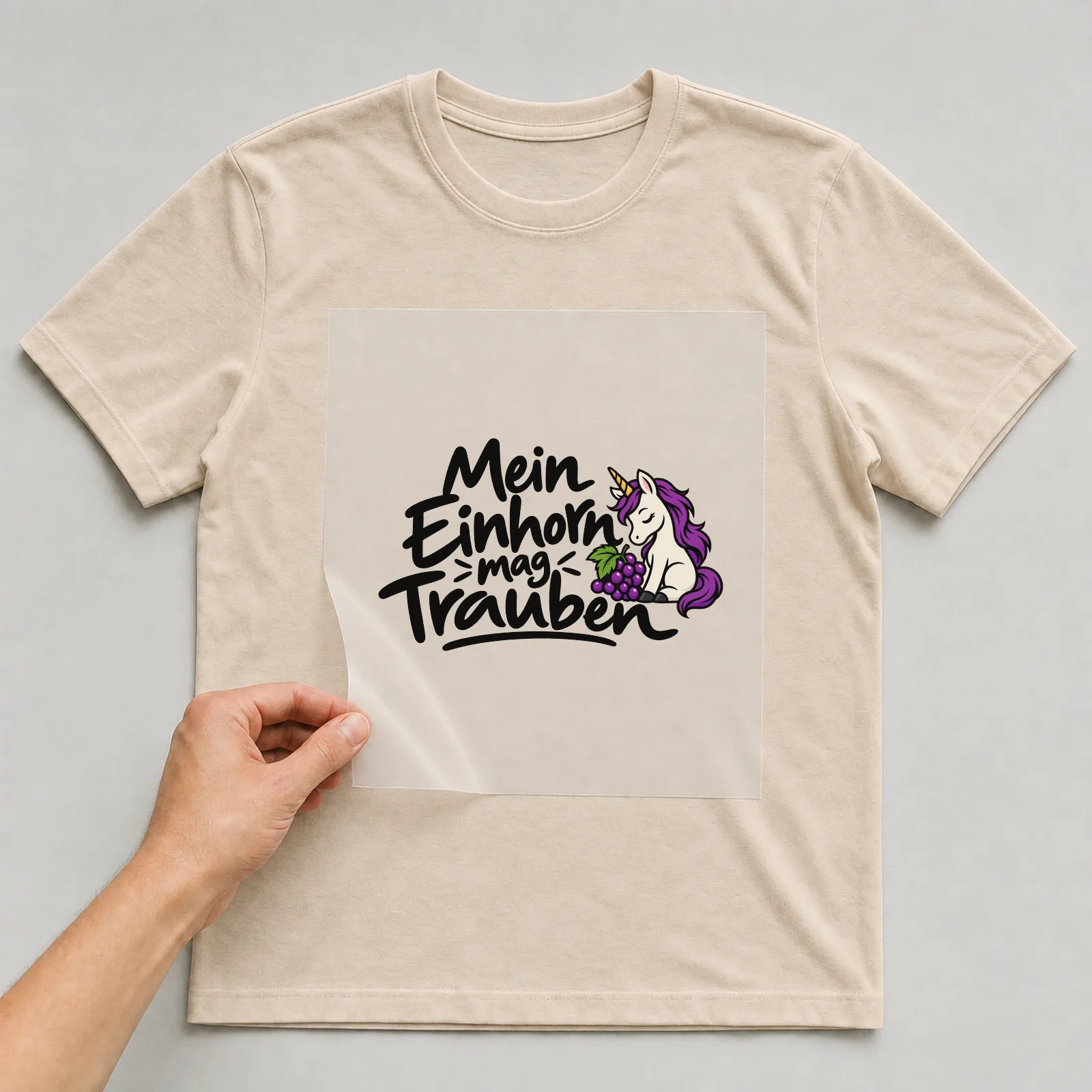 Bügelbild „Mein Einhorn mag Trauben“ auf beigem T-Shirt, Folie wird aufgelegt