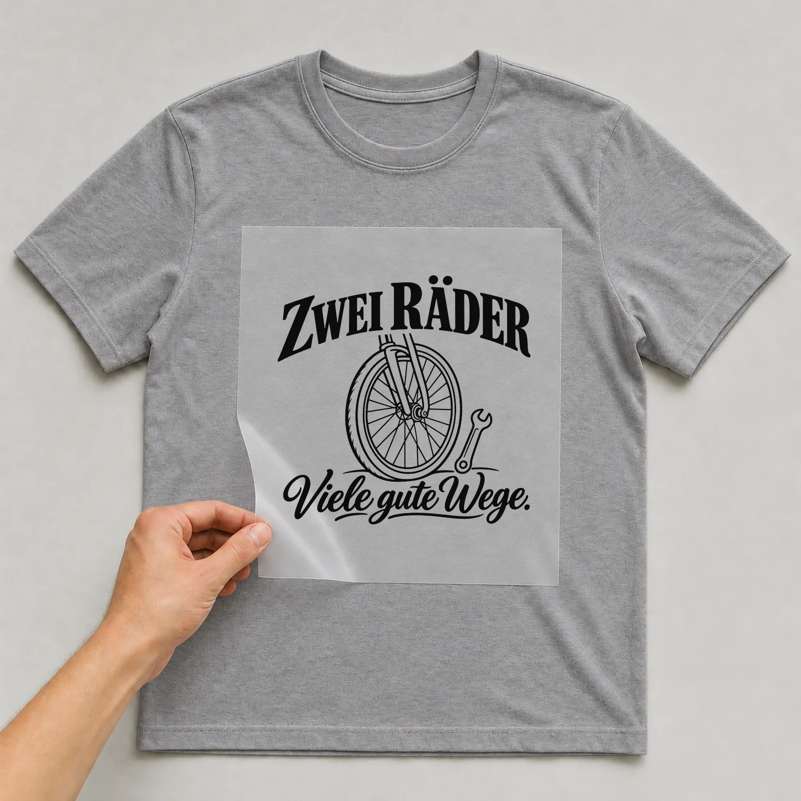 Bügelbild „Zwei Räder. Viele gute Wege.“ auf grauem T-Shirt, Folie wird aufgelegt