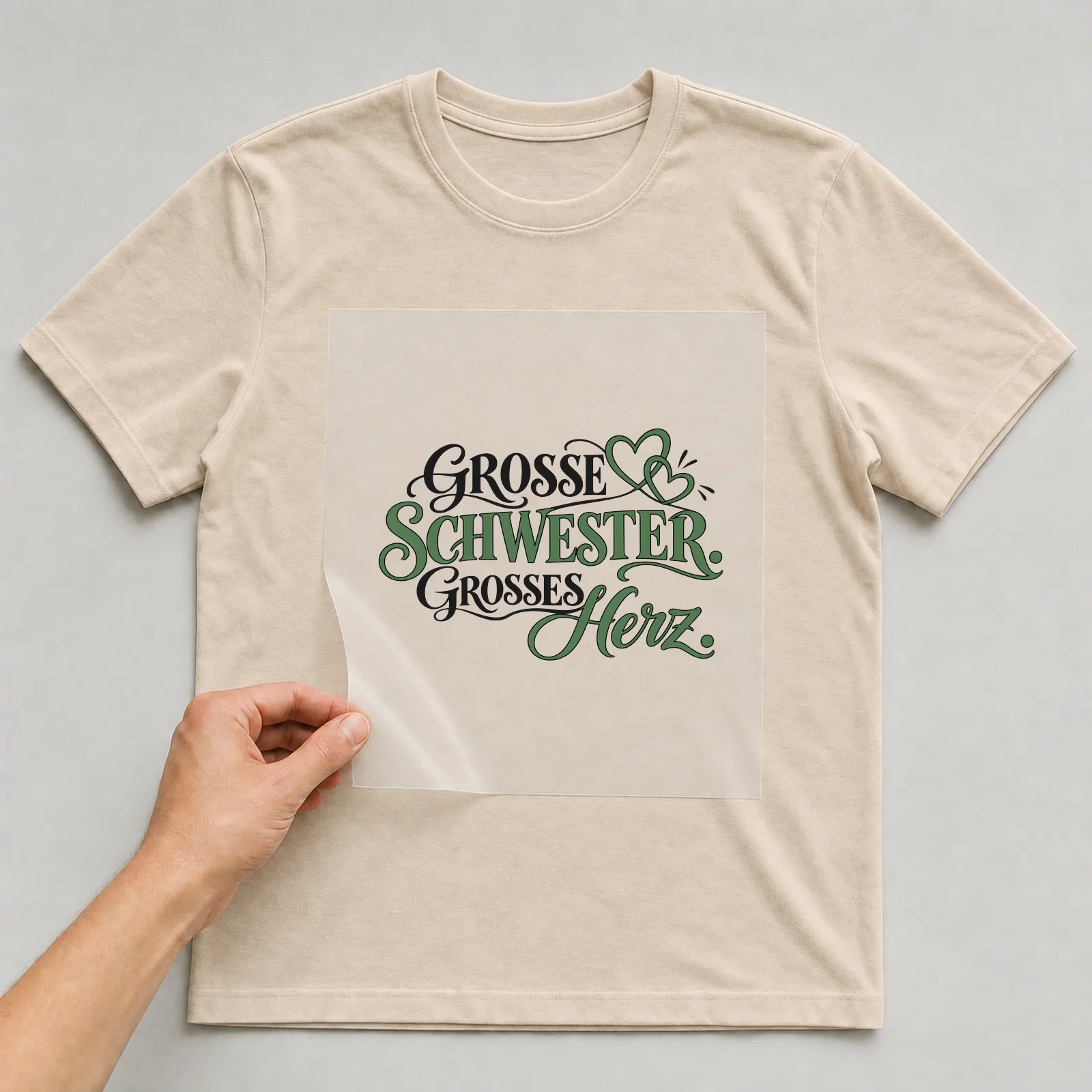 Bügelbild „Große Schwester. Großes Herz.“ auf beigem T-Shirt, Folie wird aufgelegt