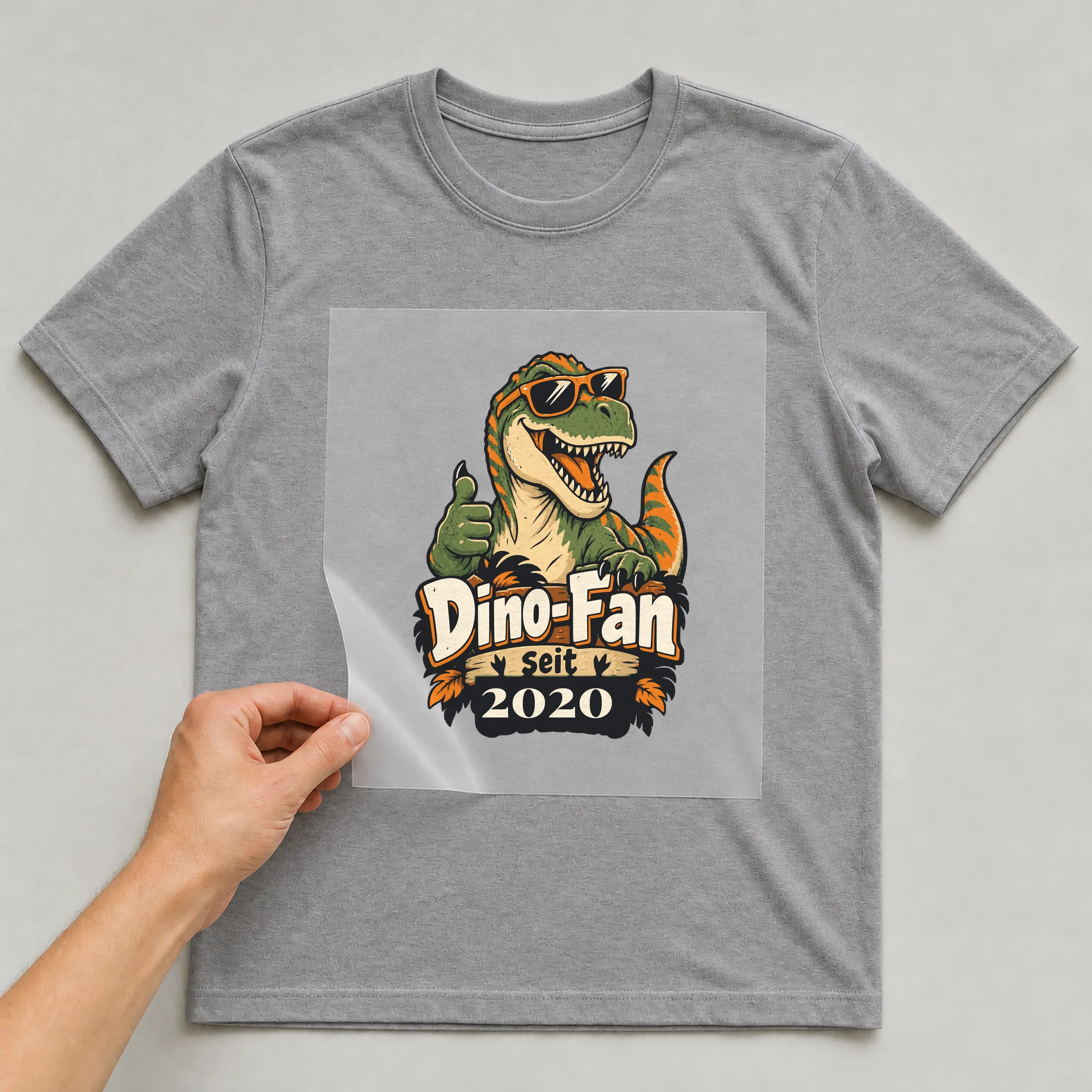 Bügelbild Dino-Fan mit Jahr auf grauem T-Shirt, Folie wird aufgelegt
